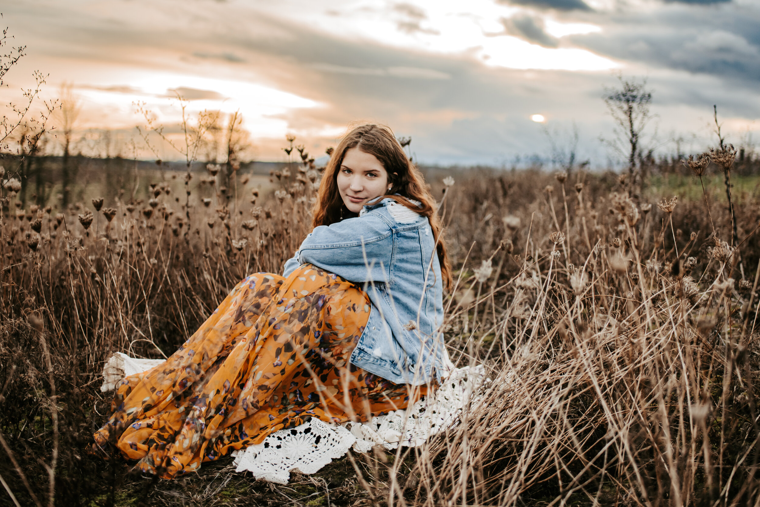 Senior girl at sunset in brown field smiling at photographer