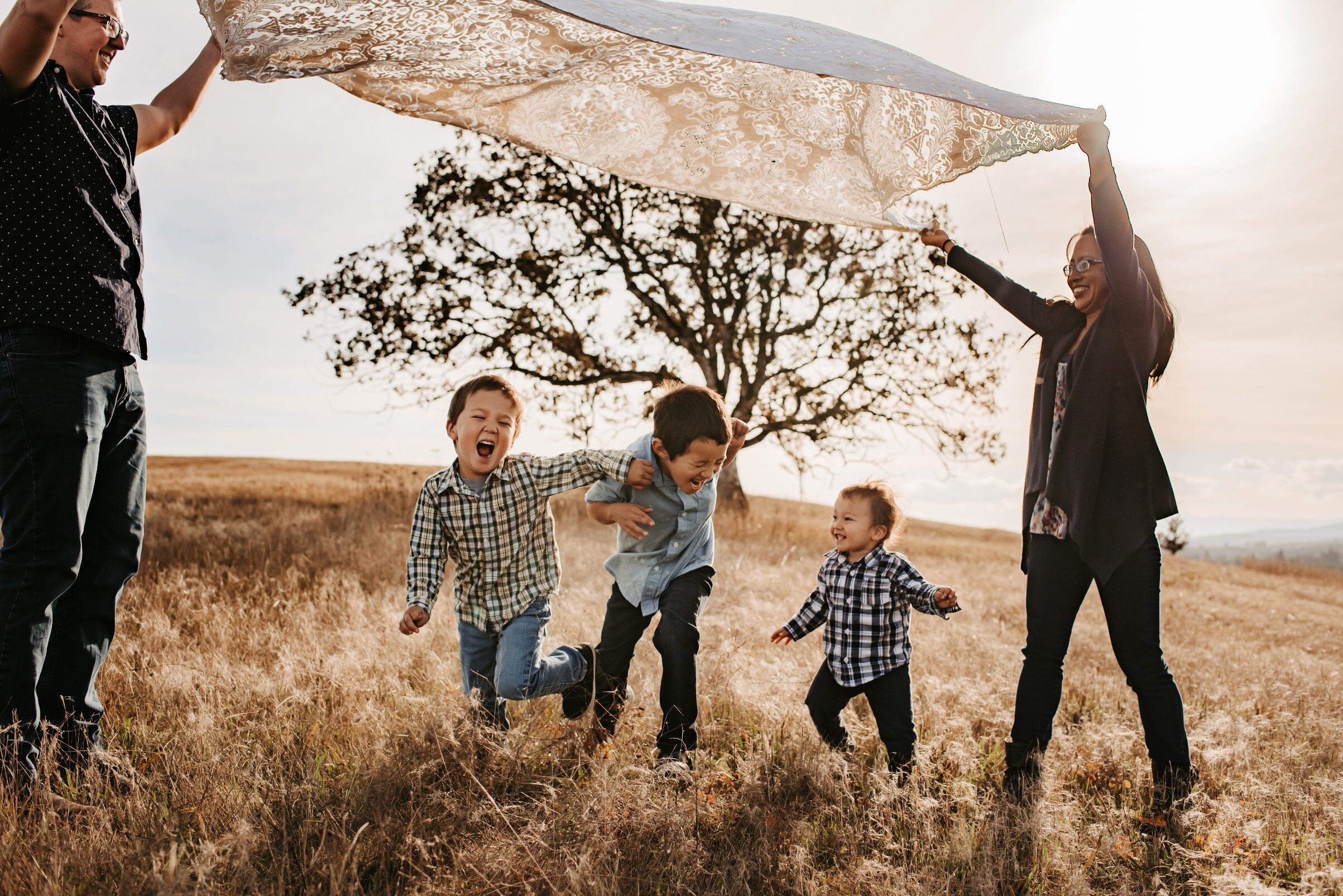 Family photographed holding blanket as kids run under it