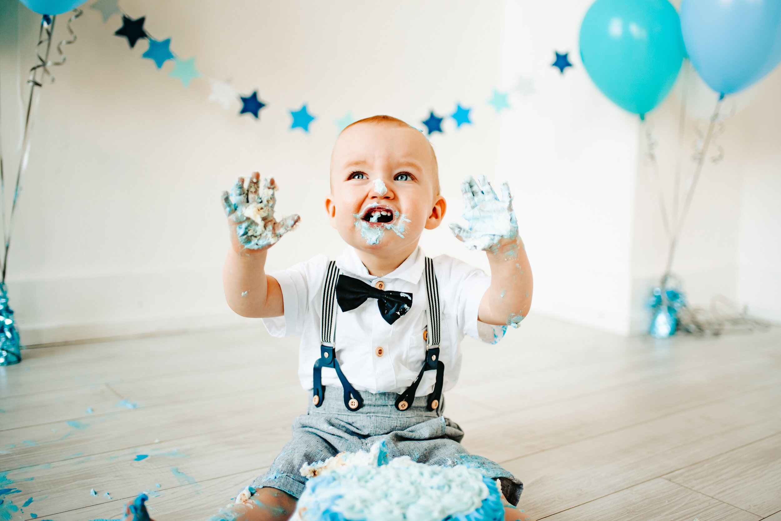 Baby boy smashing into a blue cake with both hands, frosting everywhere