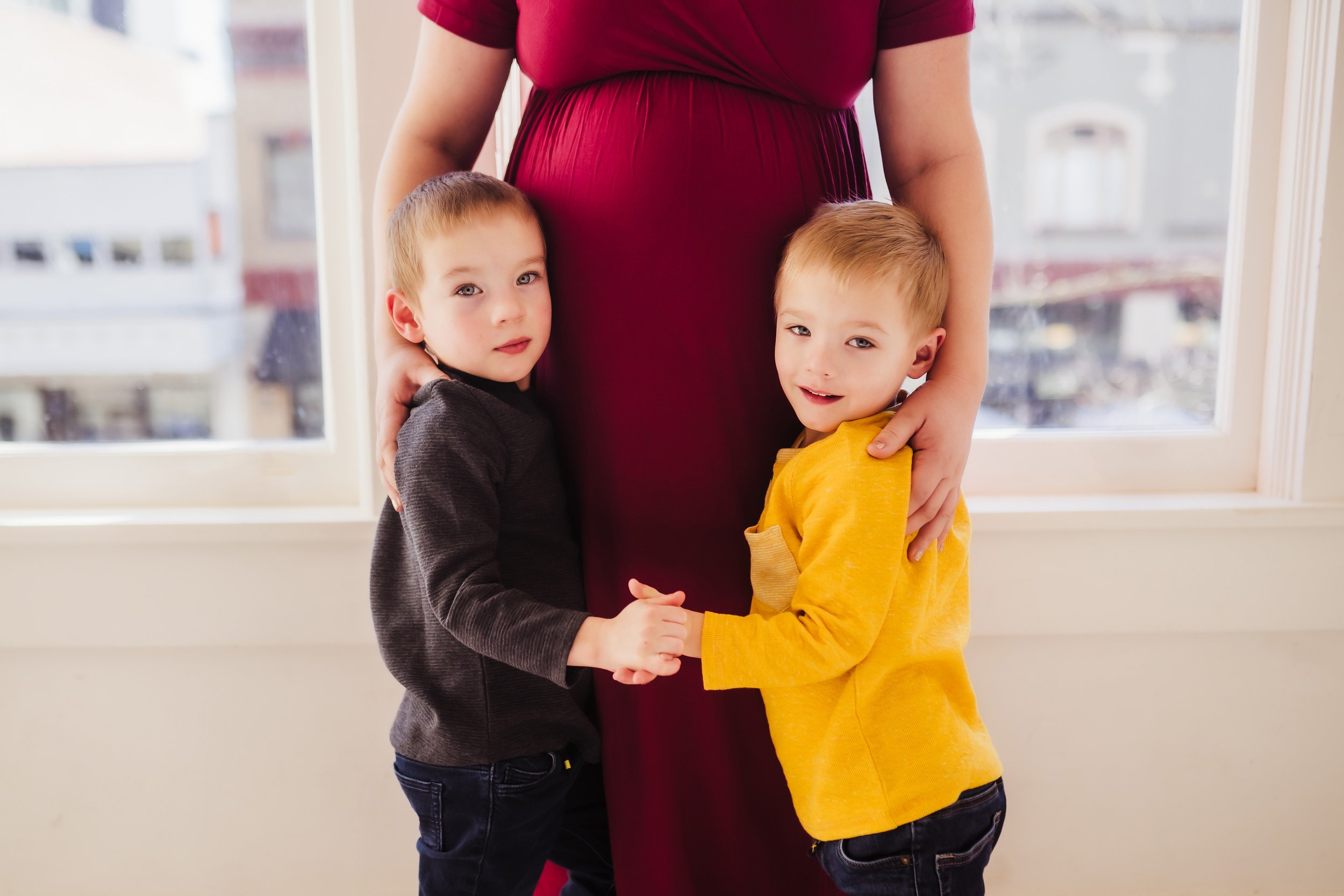 Brothers hold hands in front of their pregnant mom's belly.