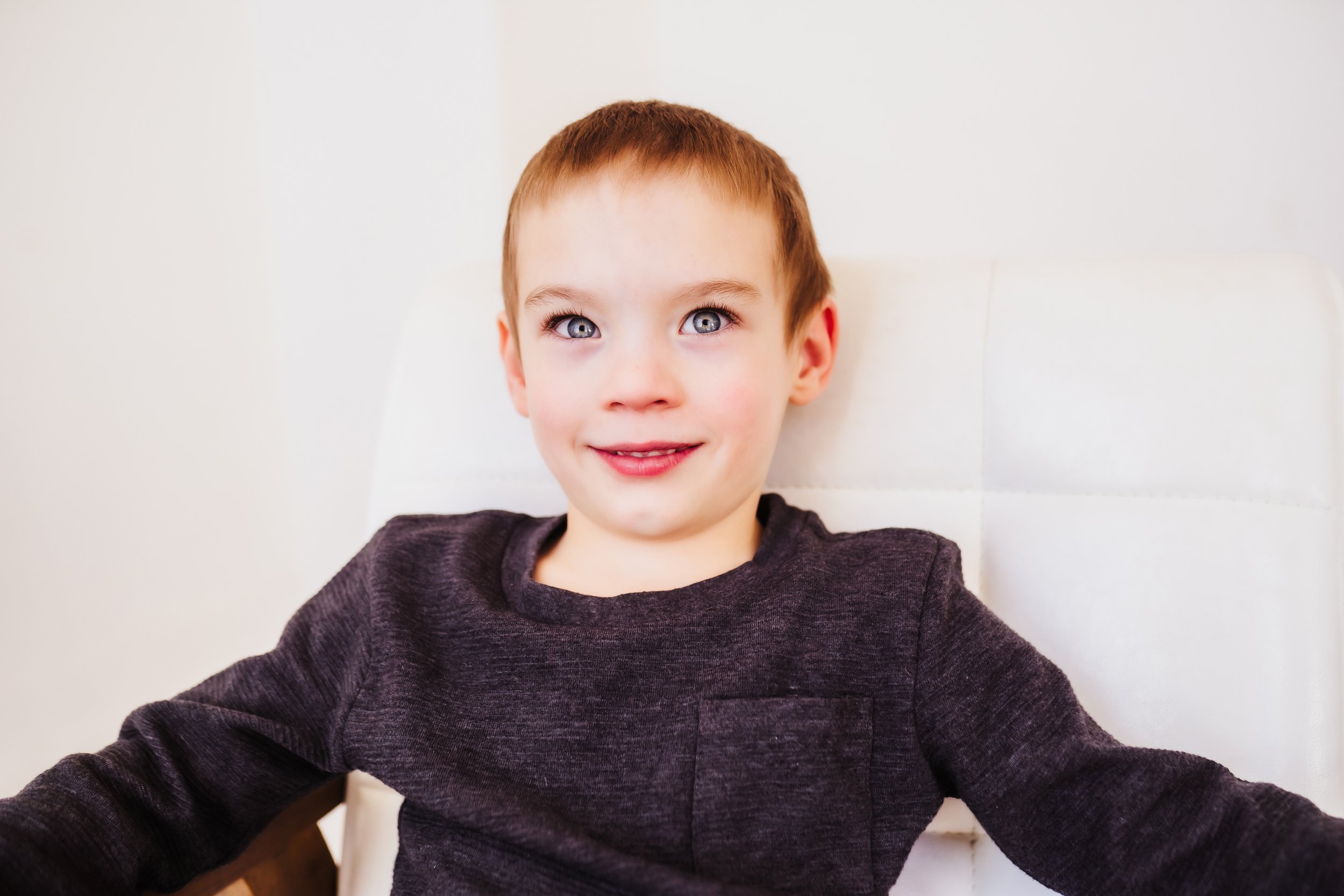 Boy smiling at photographer while sitting on white chair