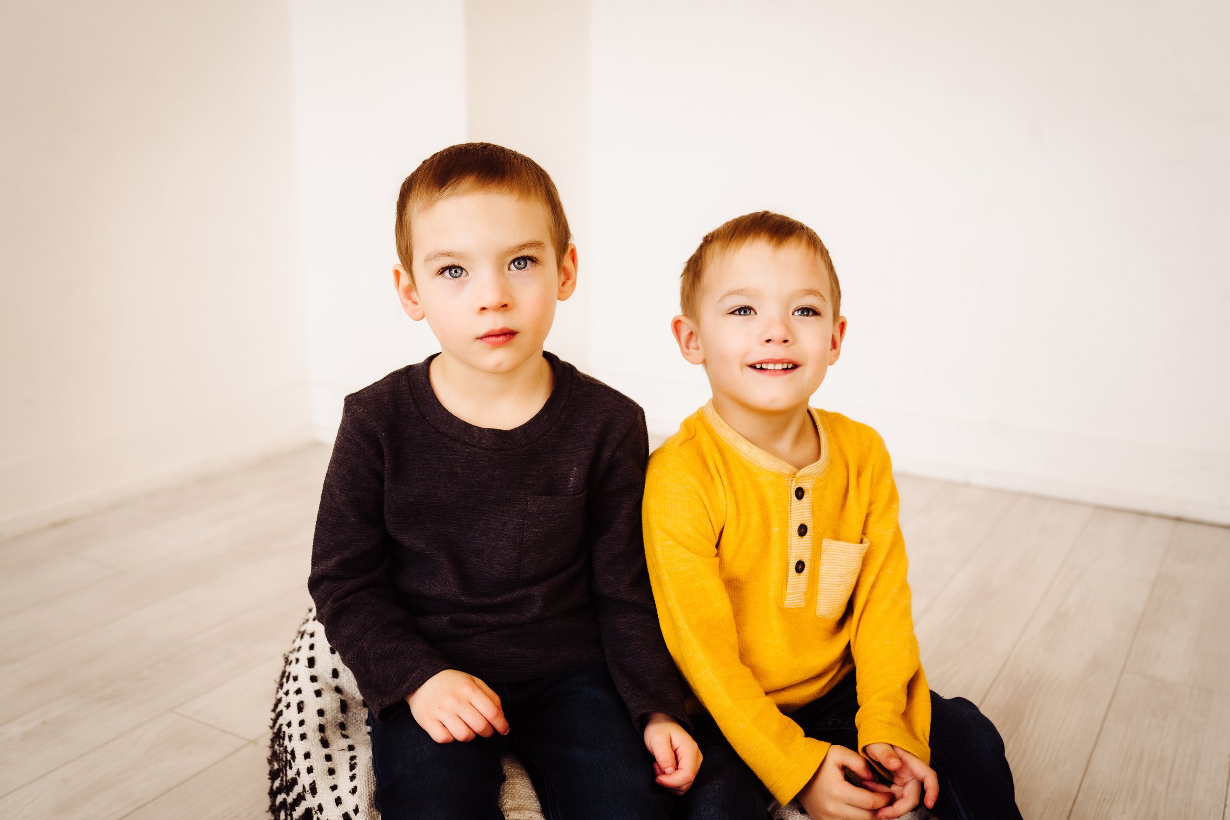 Two brothers sit on pillow and smile at photographer