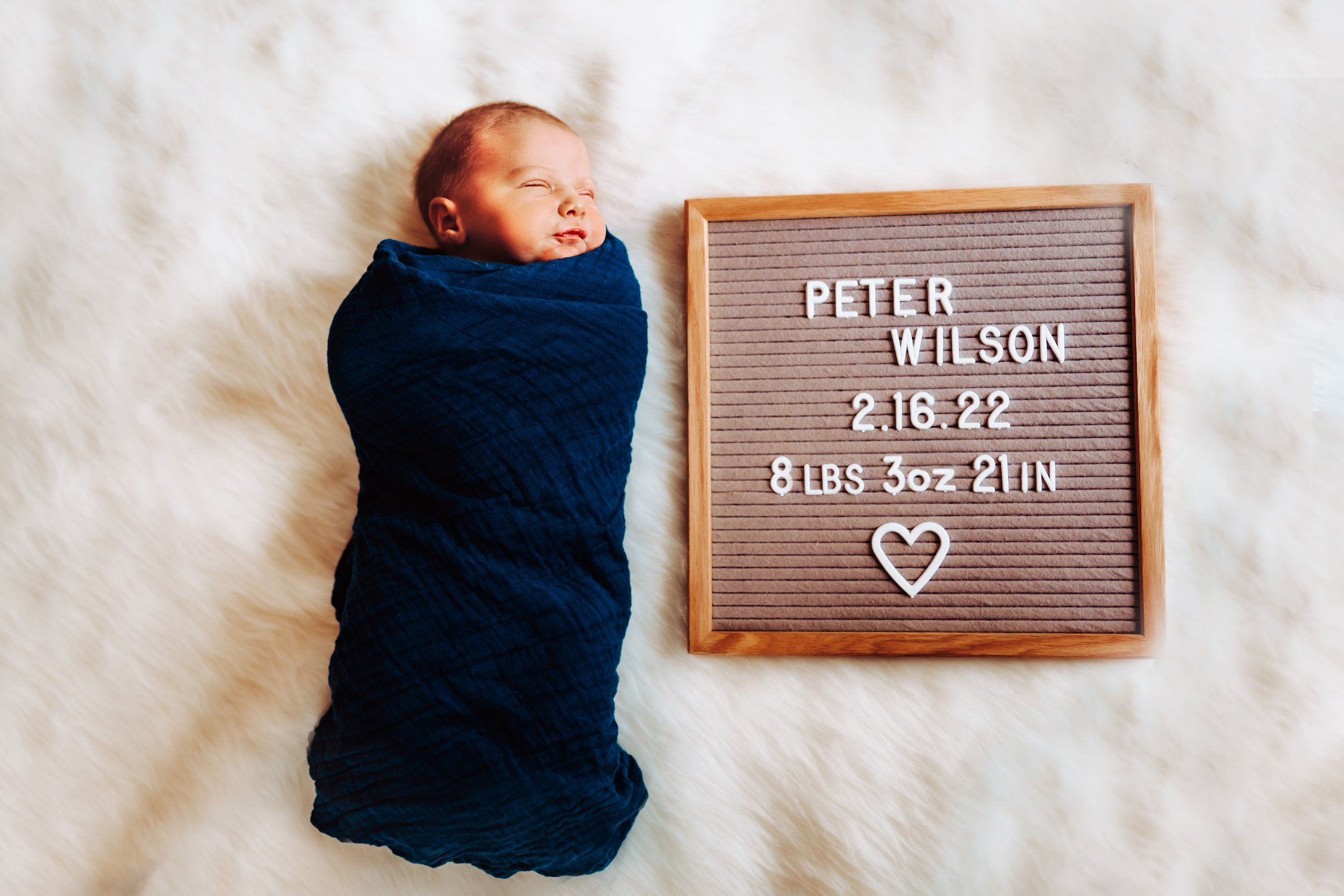 Baby Peter lays on white run with letter board of his newborn stats next to him.