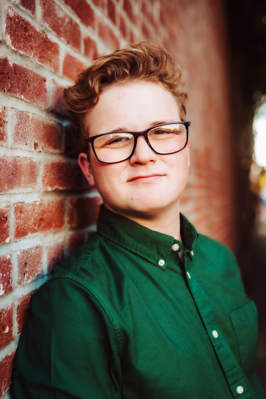 Senior leaning against a red brick wall