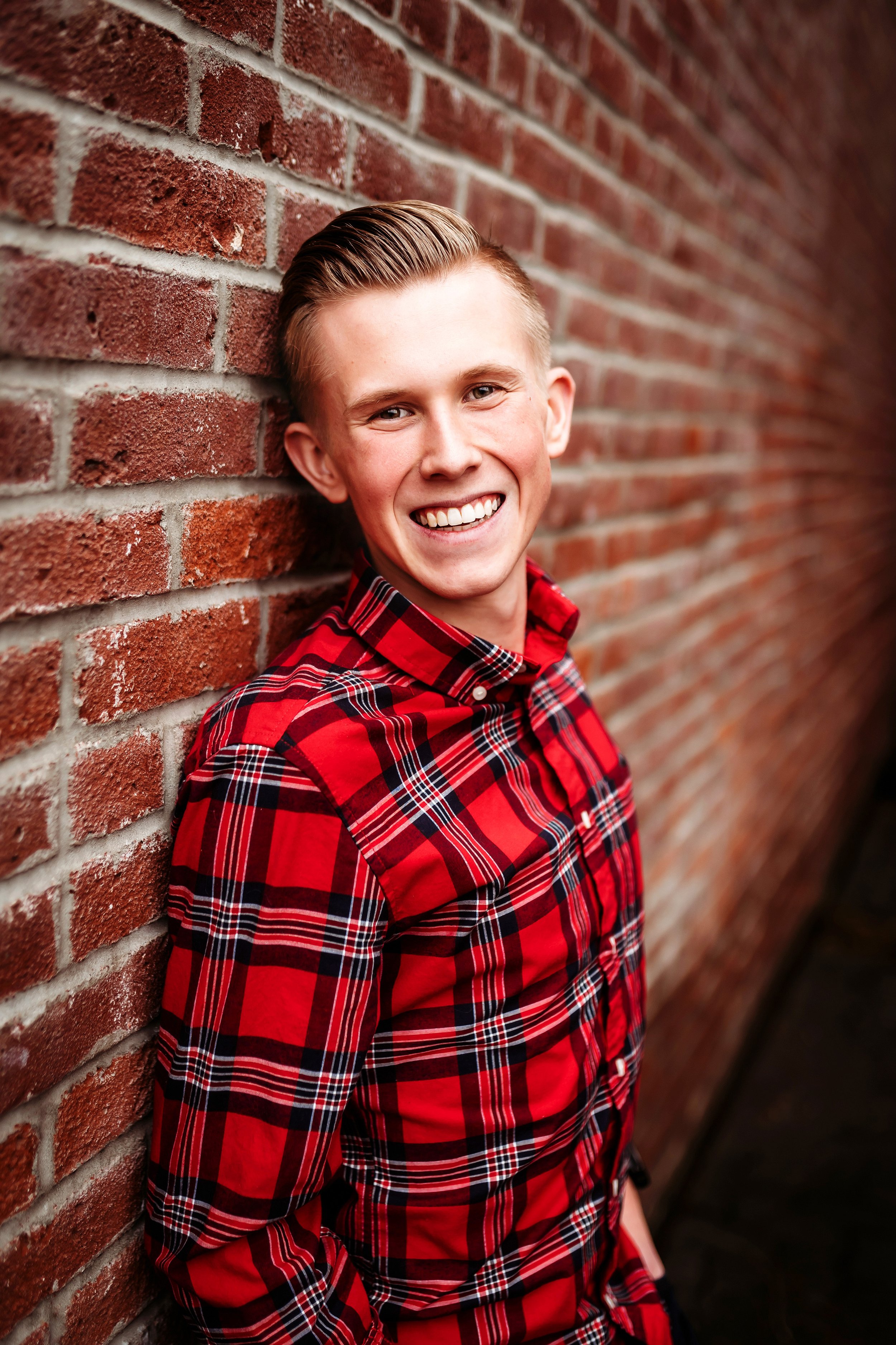 Senior leaning on red brick wall smiling at camera