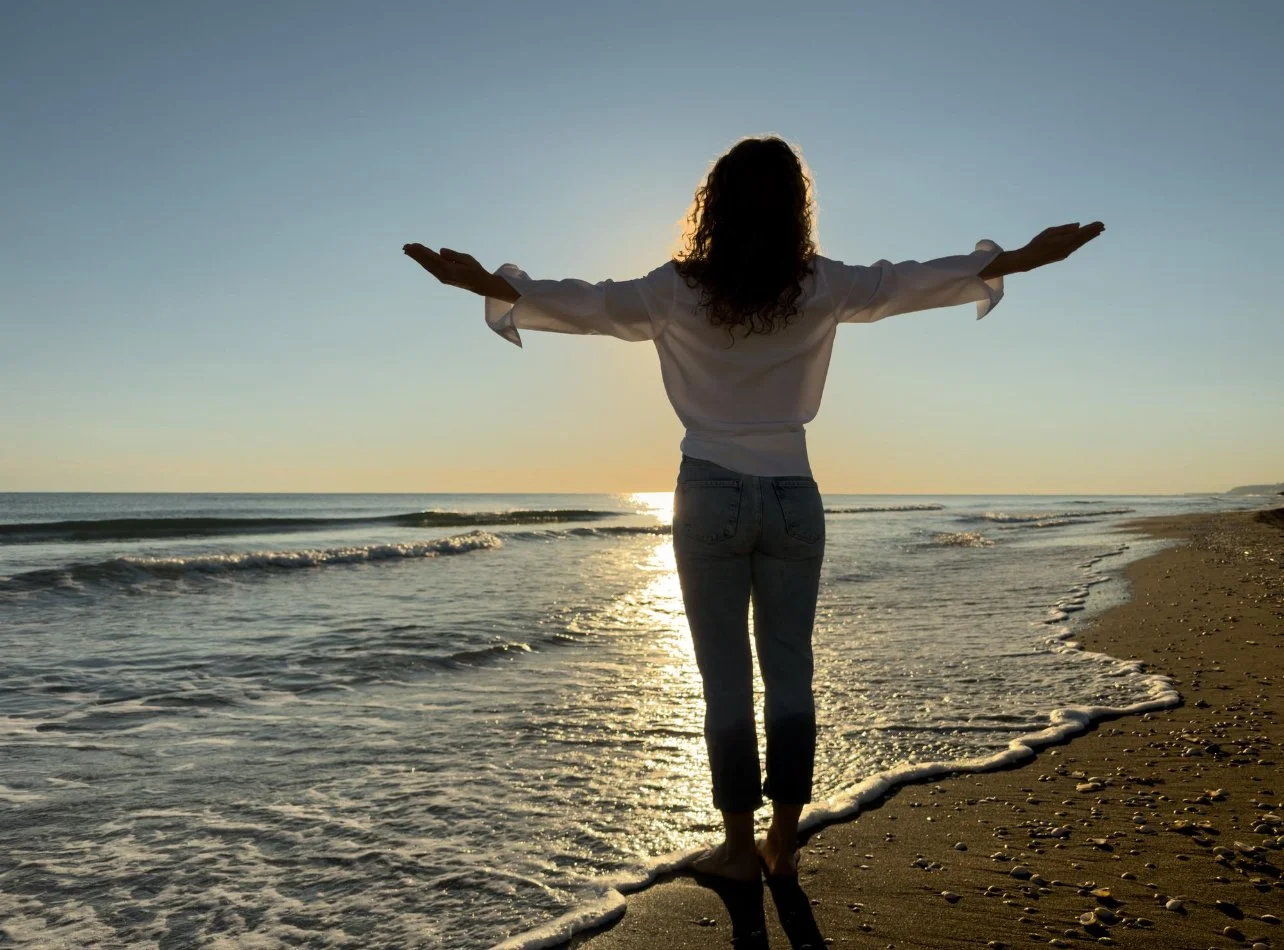 a woman standing at the shore line with her arms confidently open showing her healing from narcissitic abuse