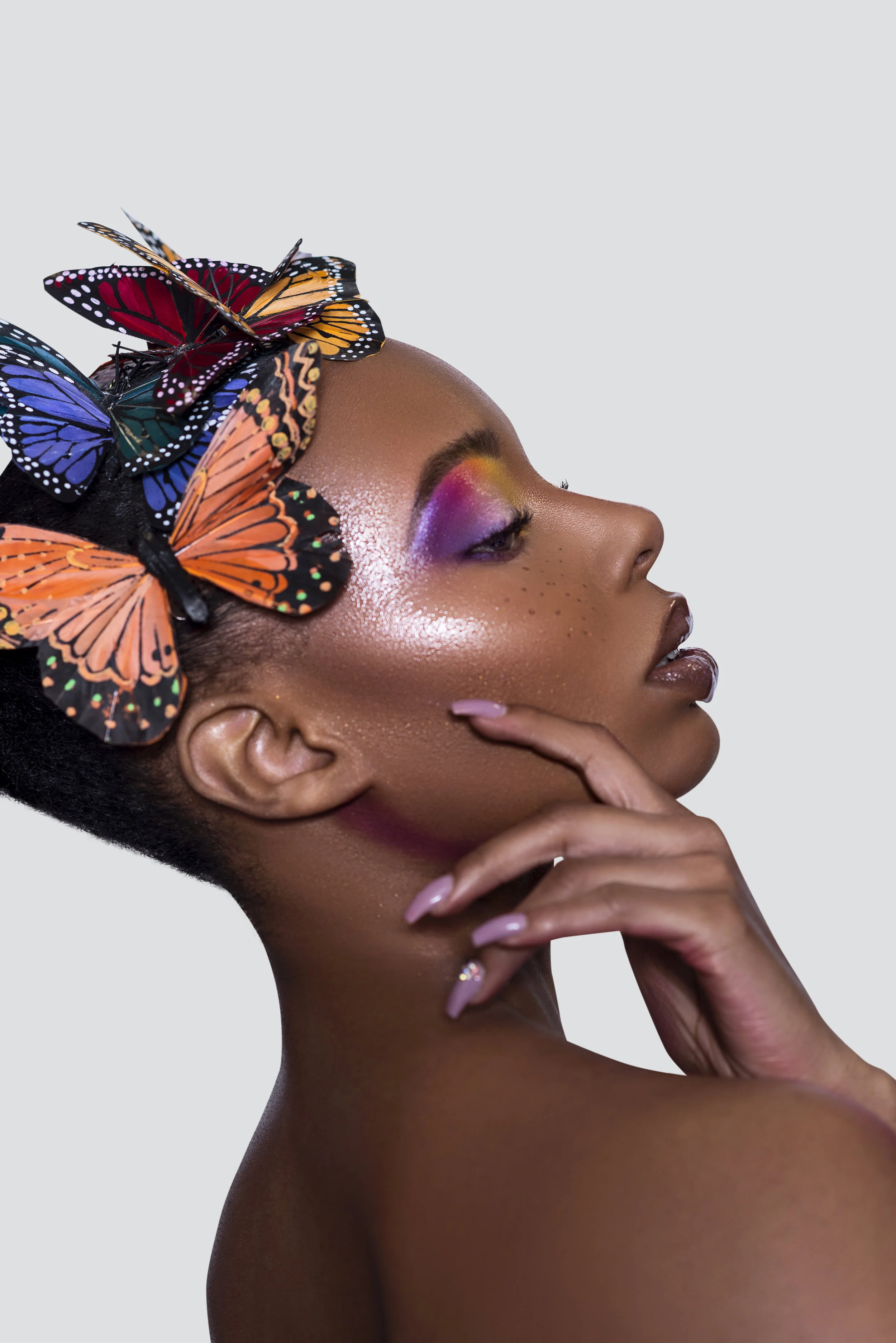 Side profile of a woman with colorful makeup and butterflies on her head.