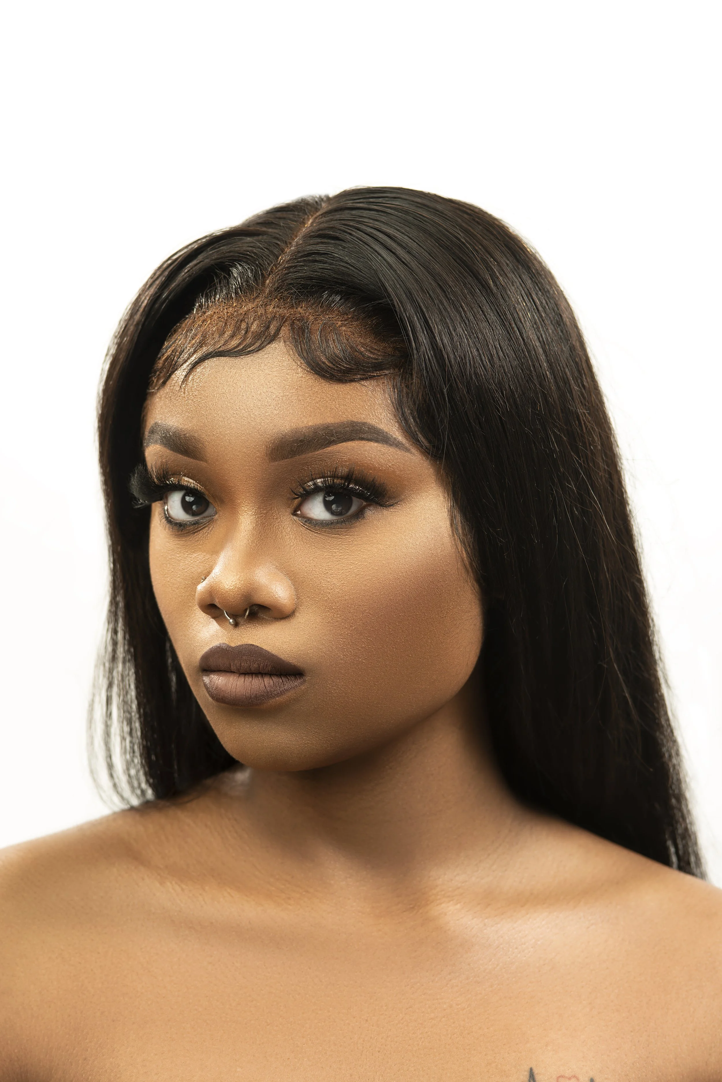 Close-up of a woman with dark straight hair, full makeup, and a nose piercing showing her face and shoulders.