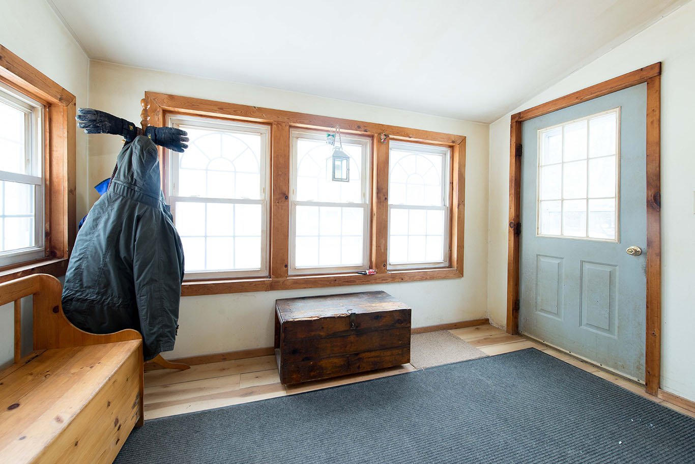 Entryway with wooden bench, coat rack with jacket, wooden chest, and multiple windows.