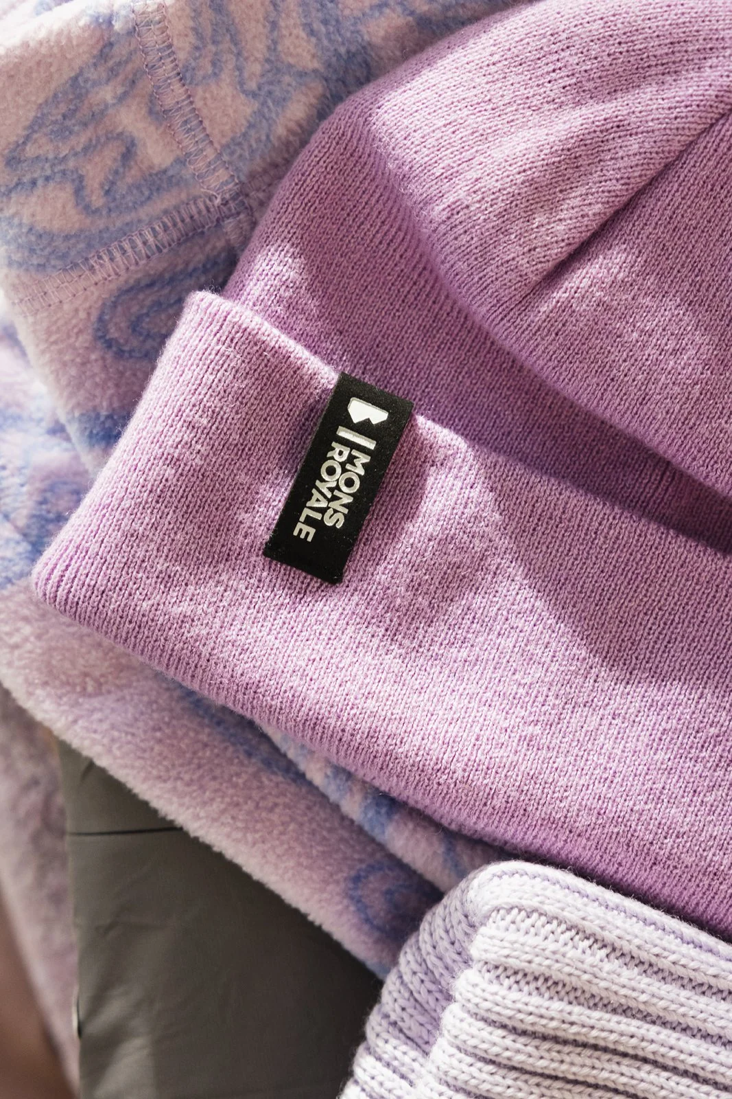 Une pile de vêtements pour enfants, comprenant un bonnet rose de The North Face, un vêtement violet à motifs, et un vêtement mauve en tissu côtelé.