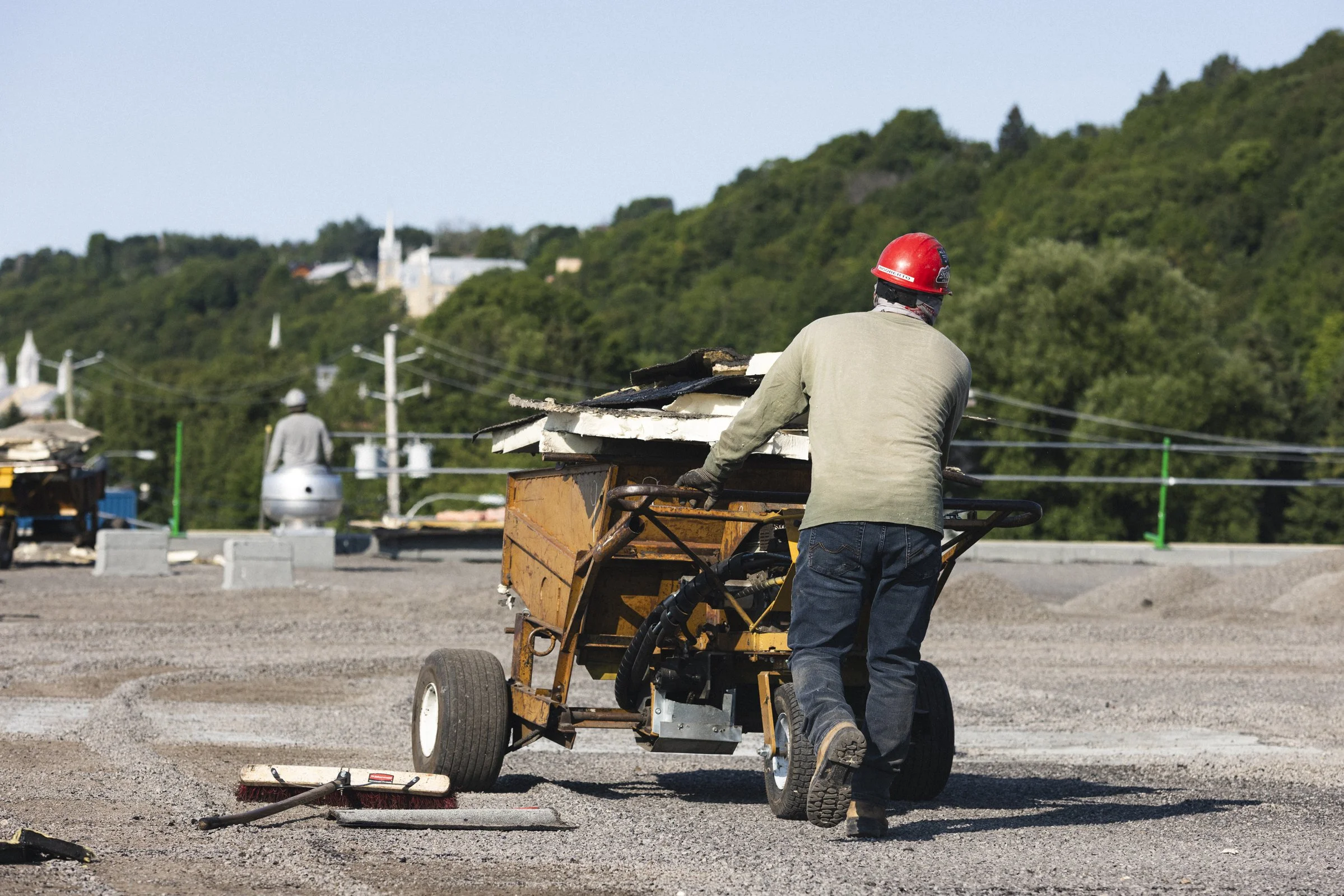 Travailleur poussant une brouette sur un chantier en extérieur, avec un casque rouge