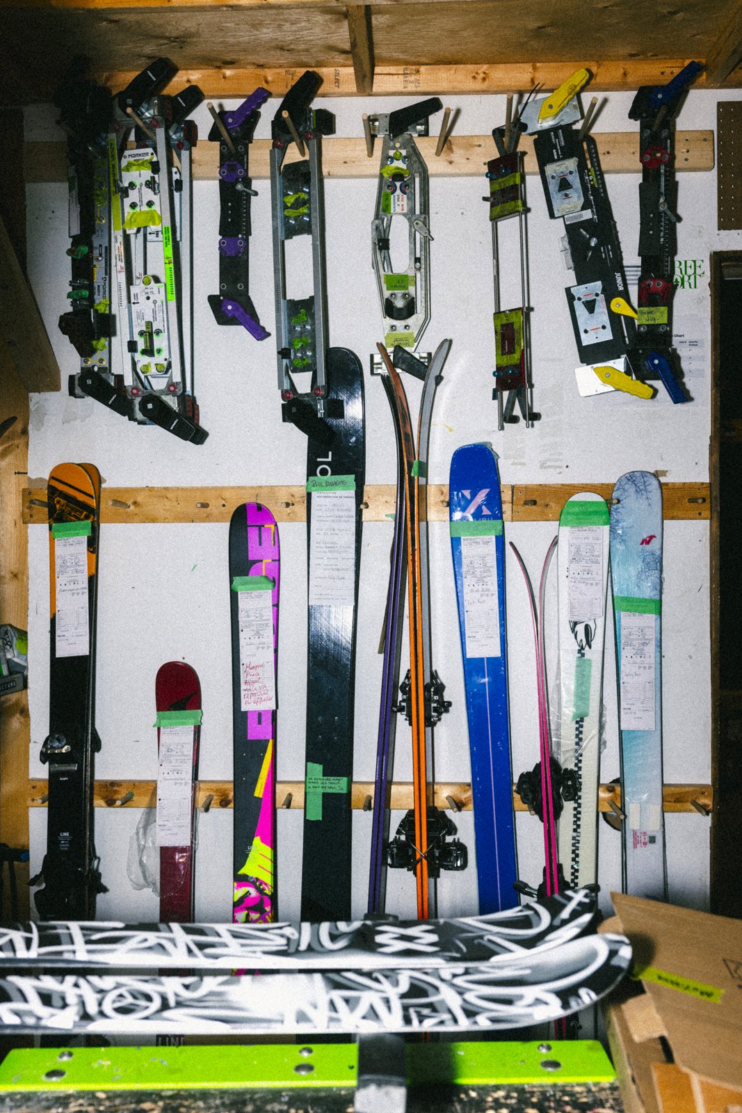 Une collection de skis et de fixations de ski accrochés à un mur, disposés de manière verticale, dans une salle ou un magasin de sport.