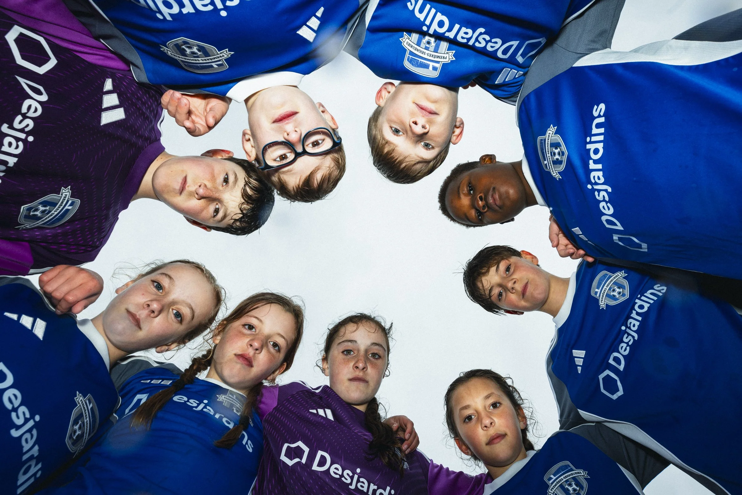 Groupe de jeunes joueurs de football formant un cercle avec la vue du sol, portant des maillots violets et bleus avec le logo de Desjardins