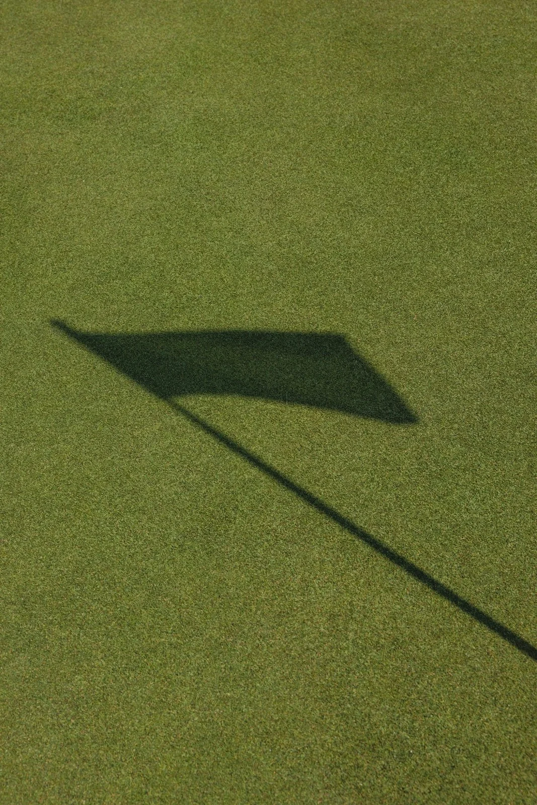 Ombre d'un drapeau sur le green d'un parcours de golf au coucher du soleil.