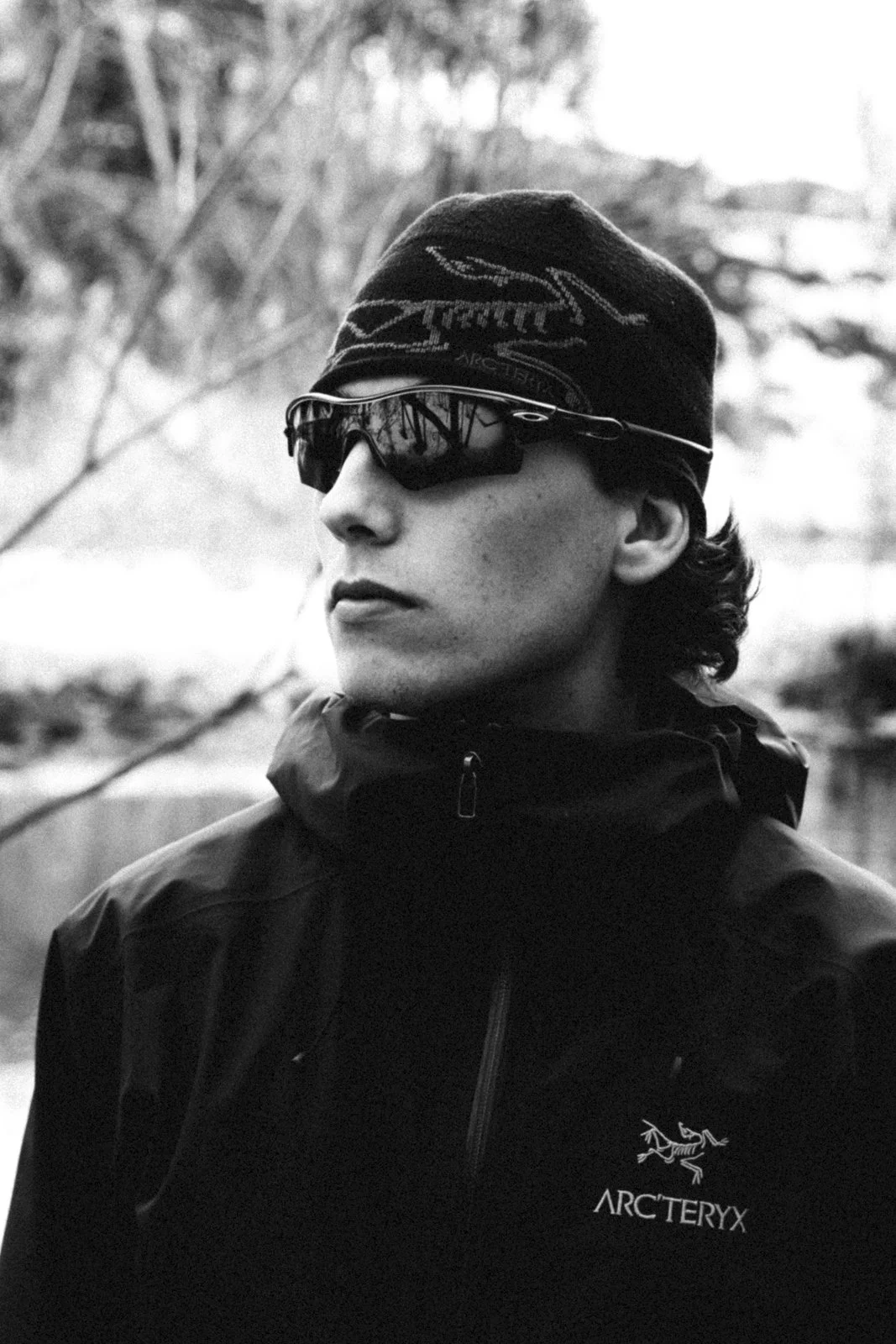 Un homme portant une casquette, des lunettes de soleil et un pull Arc'teryx en extérieur.