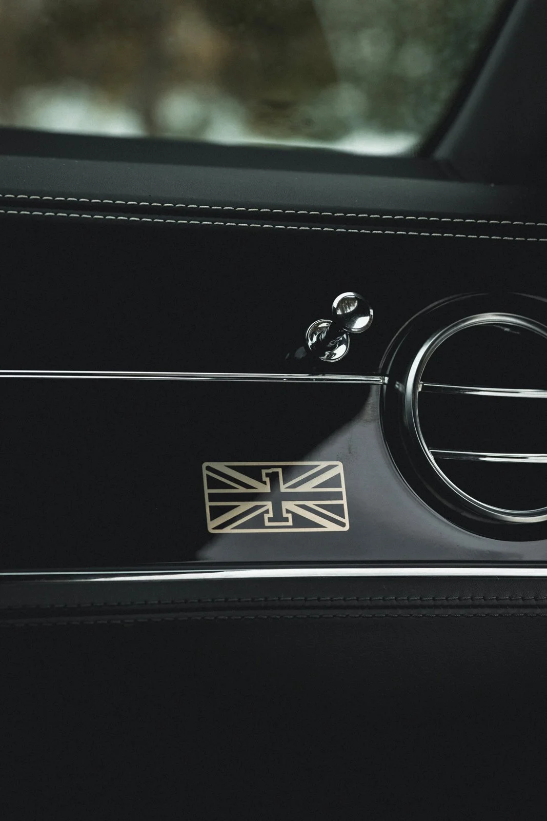 Intérieur d'une voiture avec une découpe noir, un badge avec le drapeau britannique et un chiffre 1, et une enceinte ronde en métal chromé.