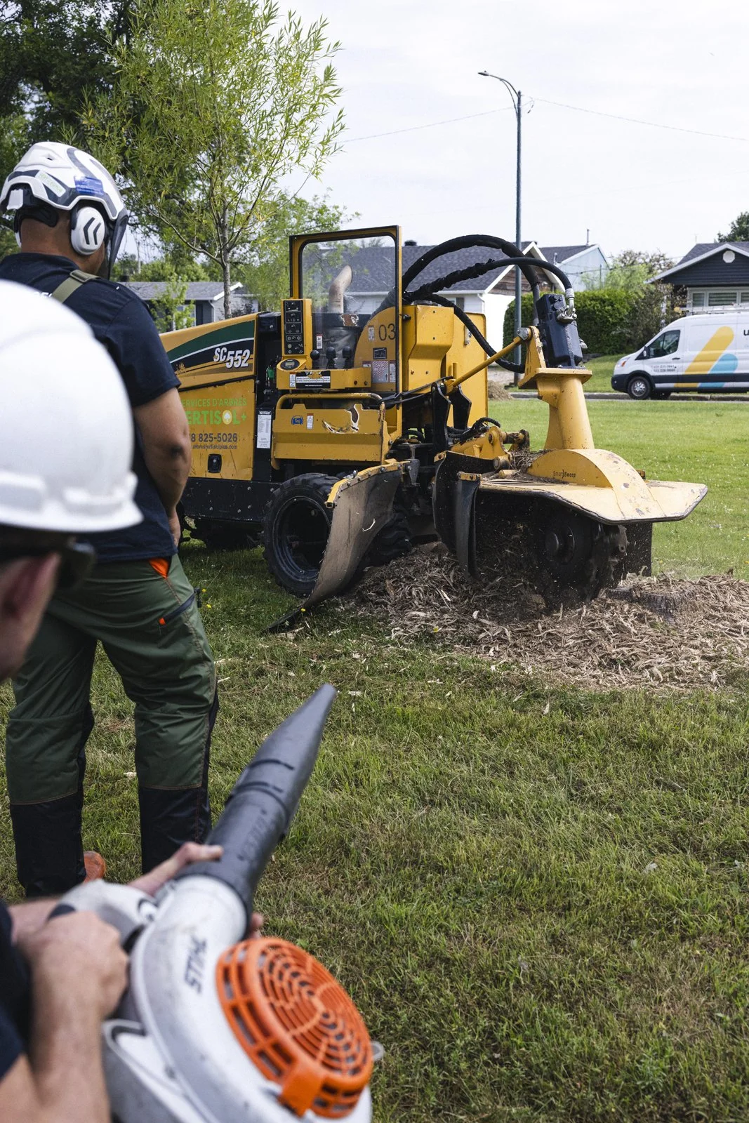 Travailleurs avec équipement de sécurité utilisant un taille-haie sur une pelouse dans un parc résidentiel.