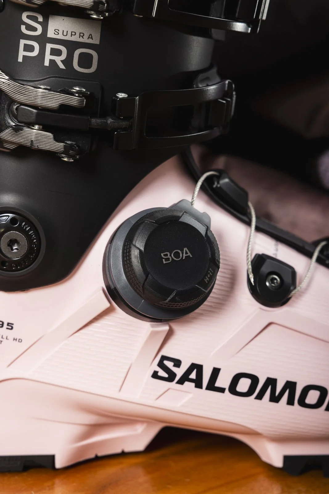 Une chaussure de ski Salomon de couleur rose avec un système de fixation, une boucle BOA, et d'autres petites boucles pour la fixation. La chaussure est noir avec le logo Salomon en noir.