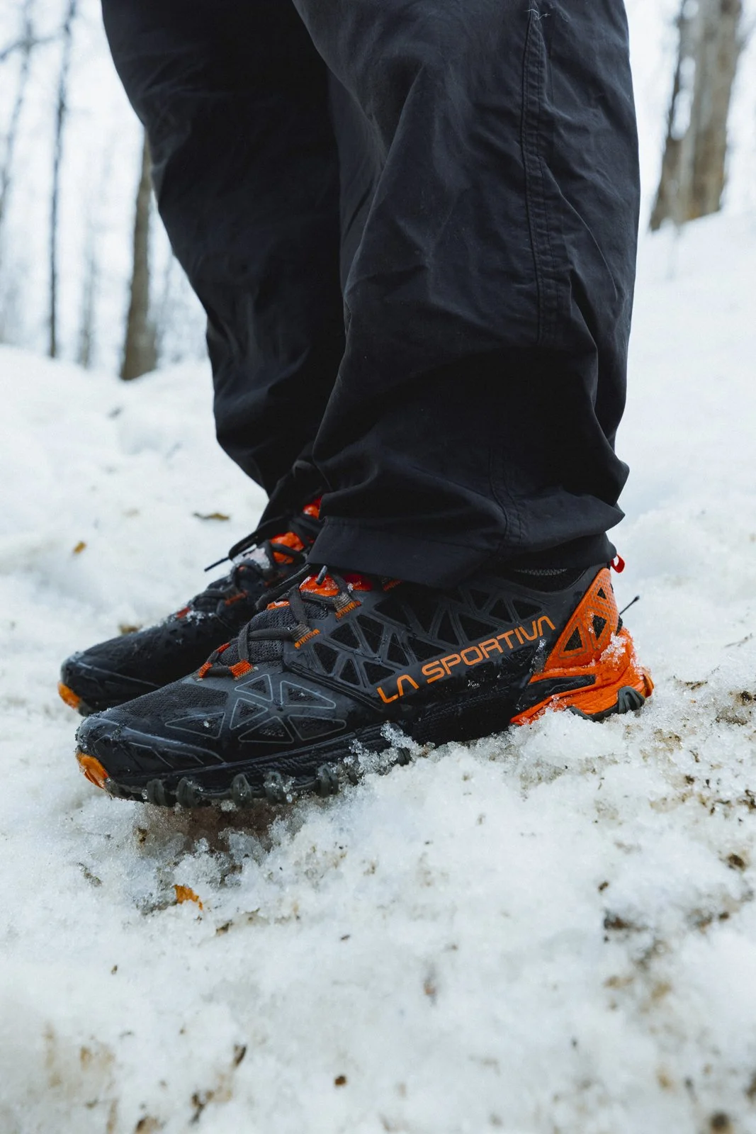 Chaussures de randonnée noires et orange de la marque La Sportiva, portant la personne dans une forêt enneigée.