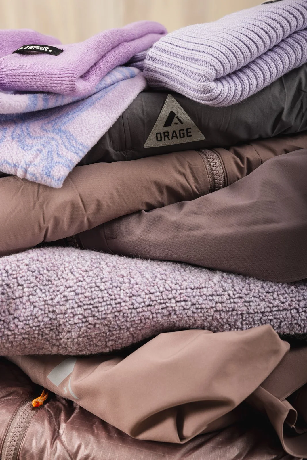 Pile de vêtements en diverses textures et couleurs, principalement en tons roses, mauves et bruns.