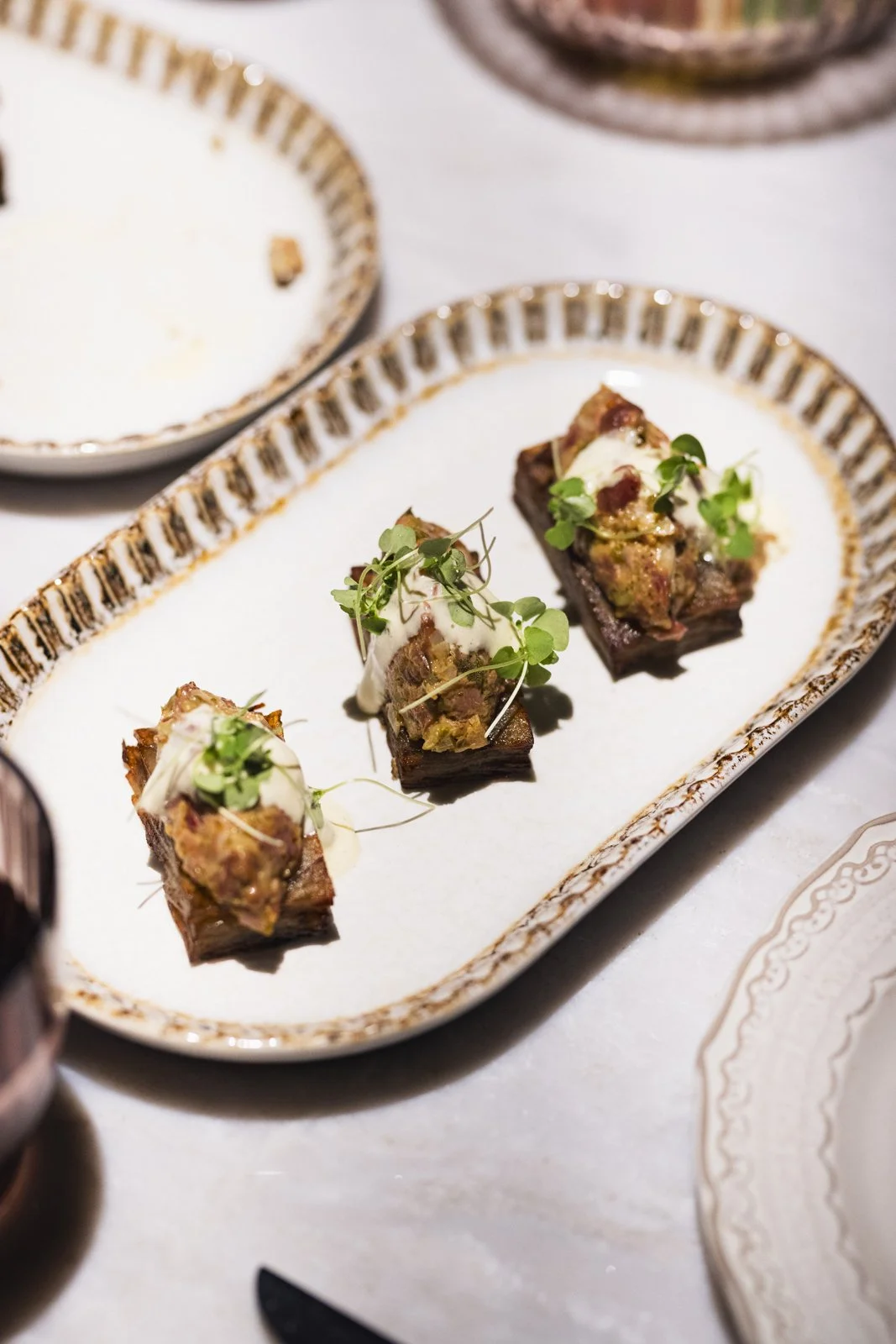 Tartare de viande avec de la crème et des micro-pousses sur une assiette décorative.