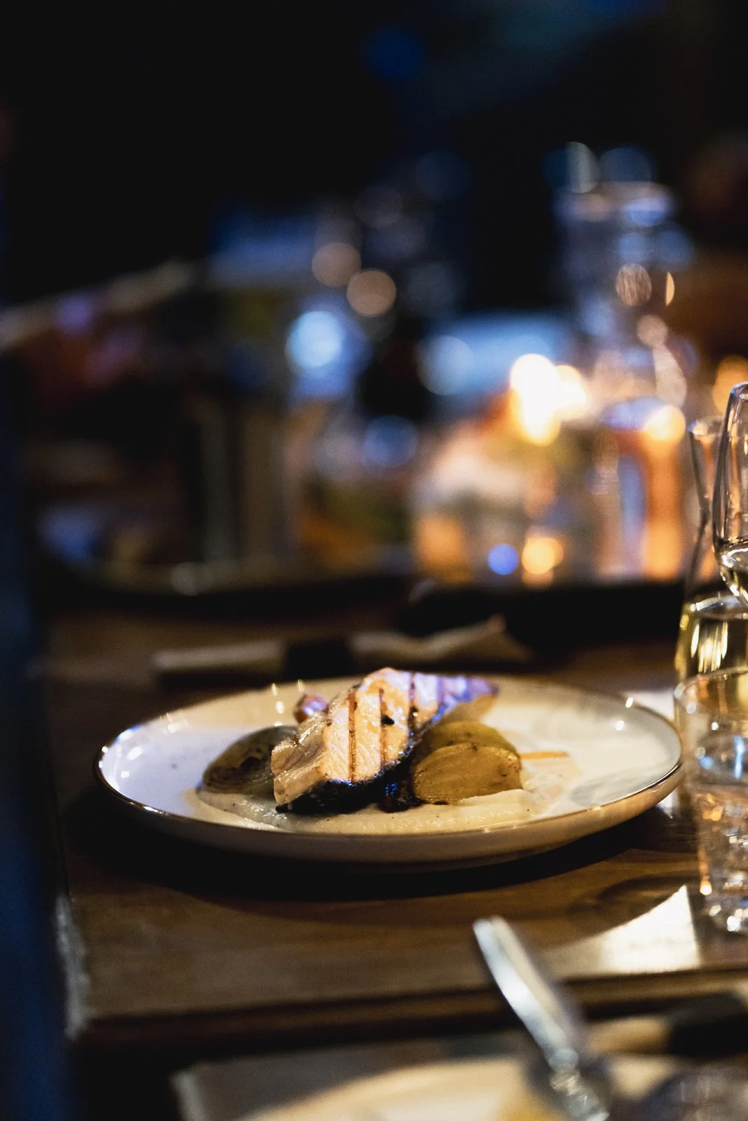 Assiette avec filet de poisson grillé et légumes, servie sur une table dans une ambiance tamisée et chaleureuse.