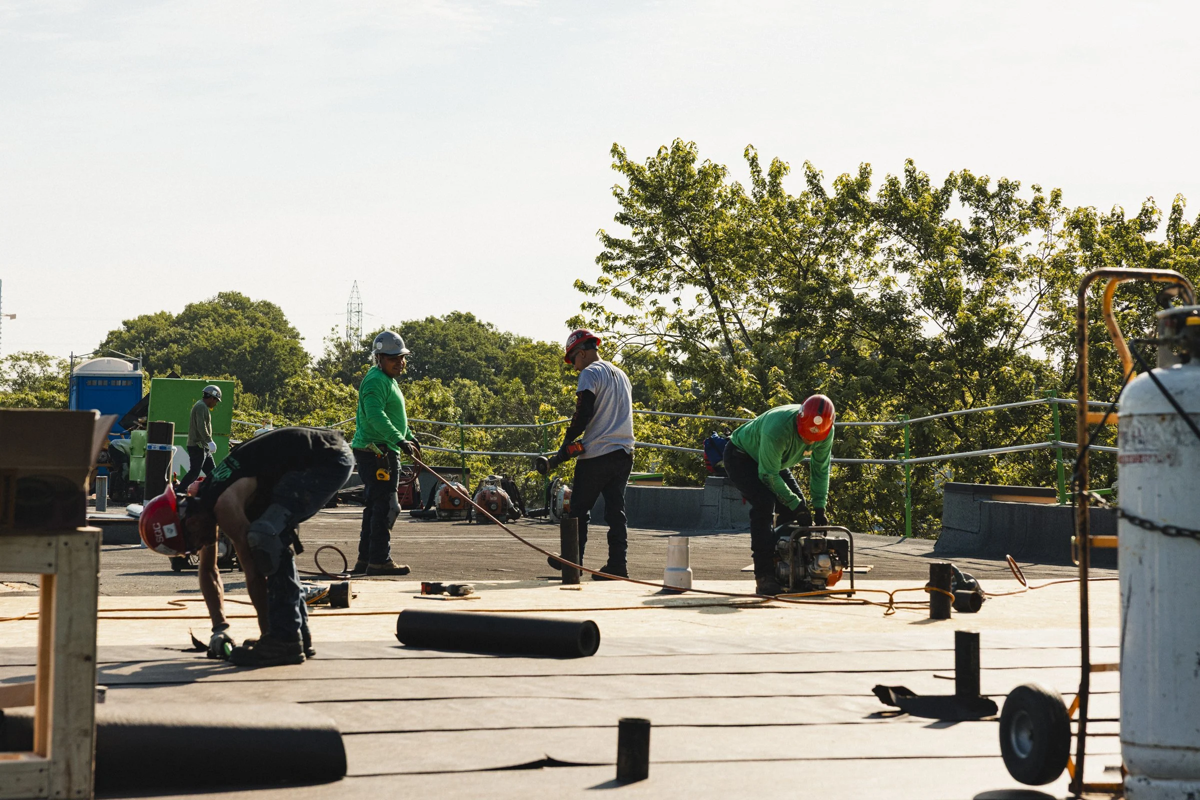 Travailleurs en sécurité portant des casques, utilisant des outils sur un toit en construction avec des arbres en arrière-plan
