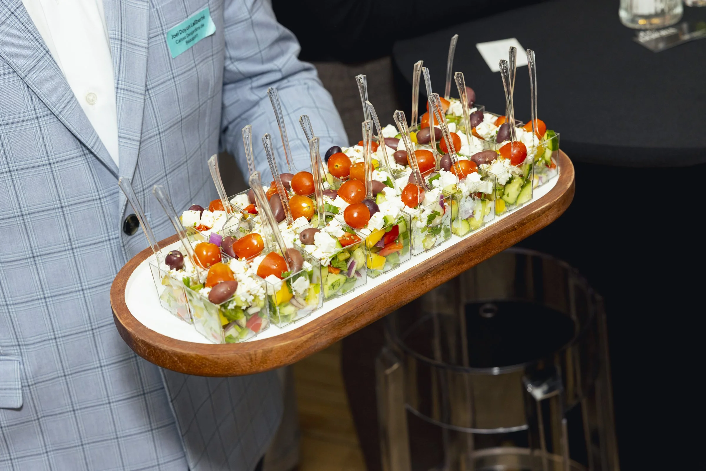 Personne tenant un plateau avec des verrines de salade de légumes, tomates cerises, olives, et fromage.