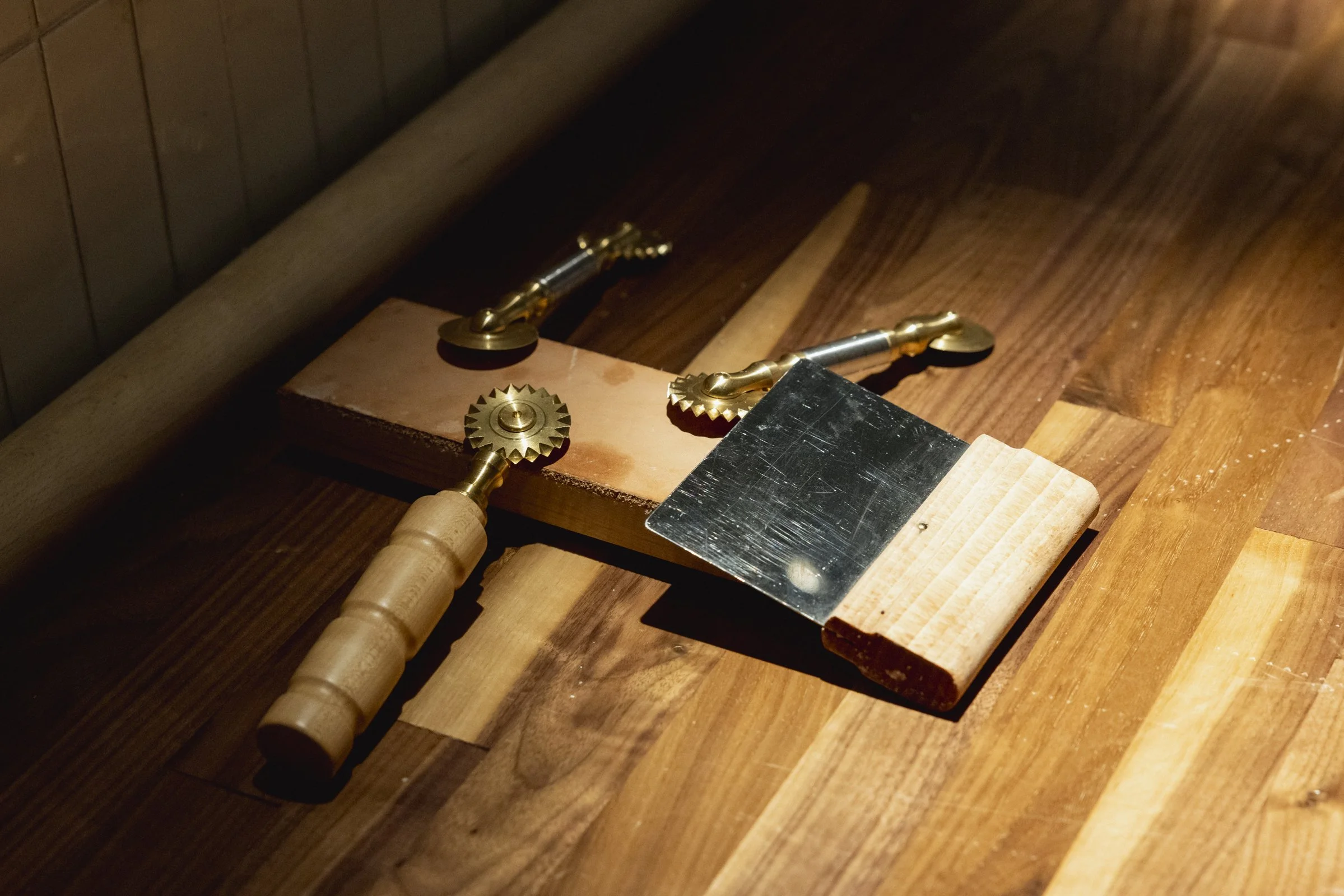 Outils de menuiserie comprenant une planche de bois, un outil en métal avec une poignée en bois, deux roues dentées en métal, et une pièce métallique plate, disposés sur un plan de travail en bois.