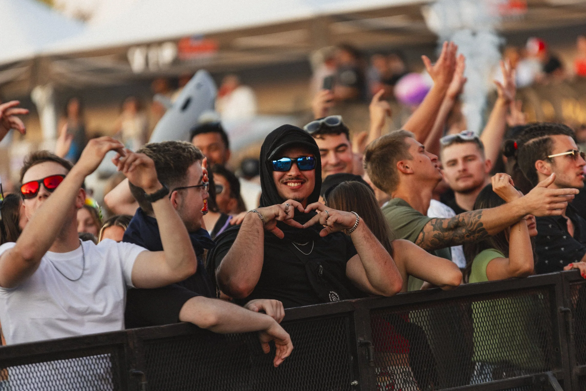 Un groupe de jeunes personnes assistant à un concert, certains faisant des gestes, souriant, portant des accessoires comme des lunettes de soleil, et montrant différents comportements de fête.