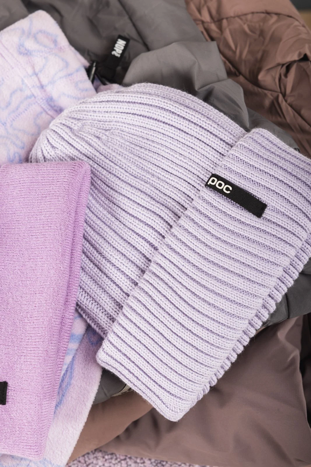 Gants, bonnet et foulard de couleur violette et rose sur un tapis. La plupart des articles portent une étiquette noire avec le mot "poc".