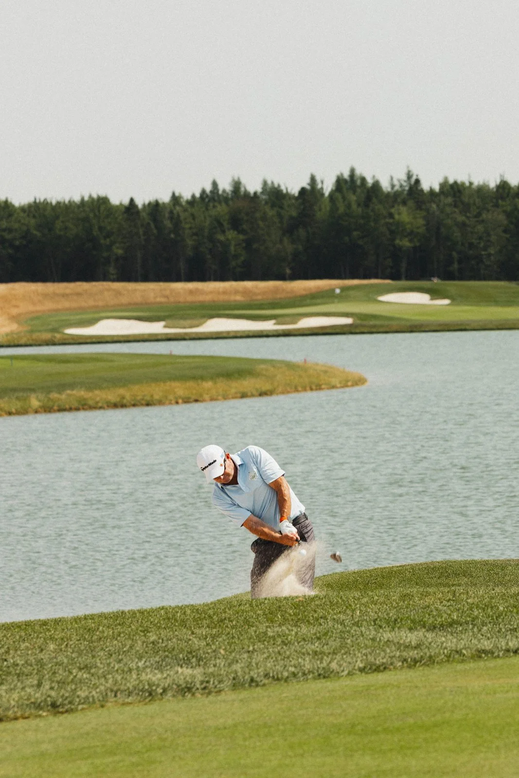 Un golfeur en train de jouer dans un paysage de golf avec de l'eau et des zones de bunkers, sous un ciel clair.