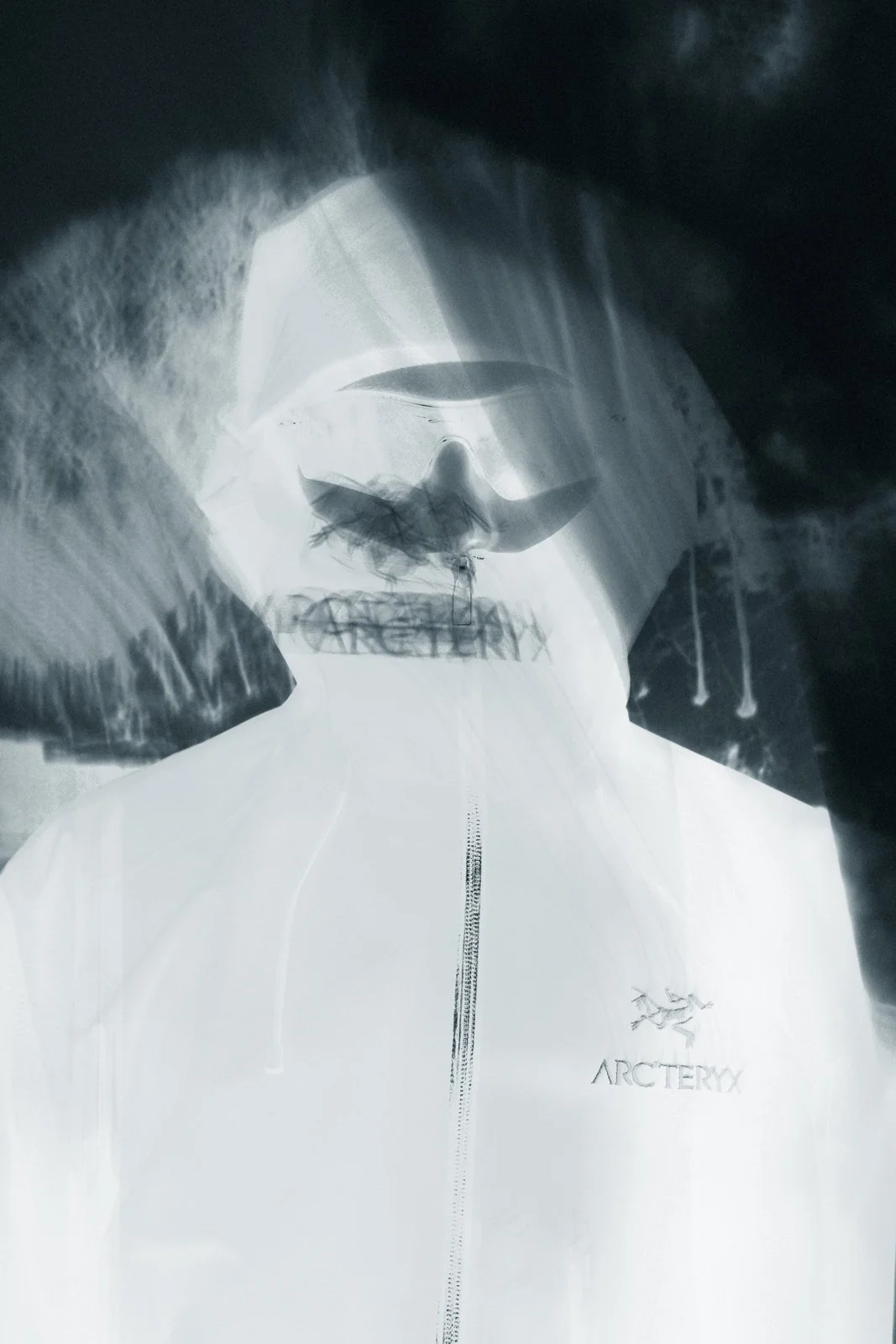 Une personne portant une veste de marque Arc'teryx, vue à travers une surface réfléchissante ou translucide, créant un effet artistique et abstrait.