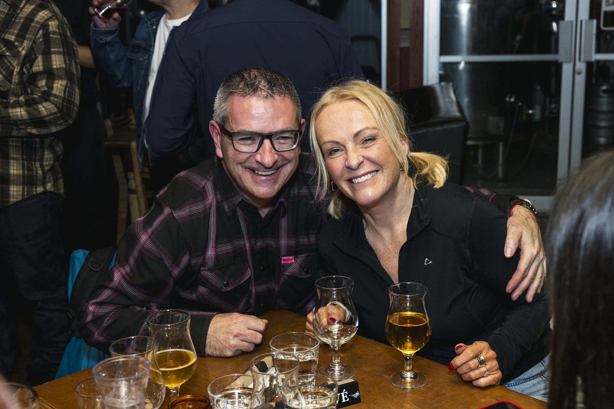 Un homme et une femme souriants assis à une table de bar, tenant des verres d'alcool, lors d'une soirée entre amis.
