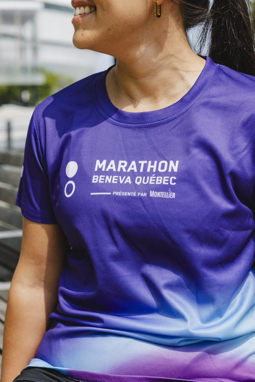 Portrait d'une femme souriante portant un t-shirt violet avec l'inscription 'Marathon Bénéva Québec' lors d'une course.
