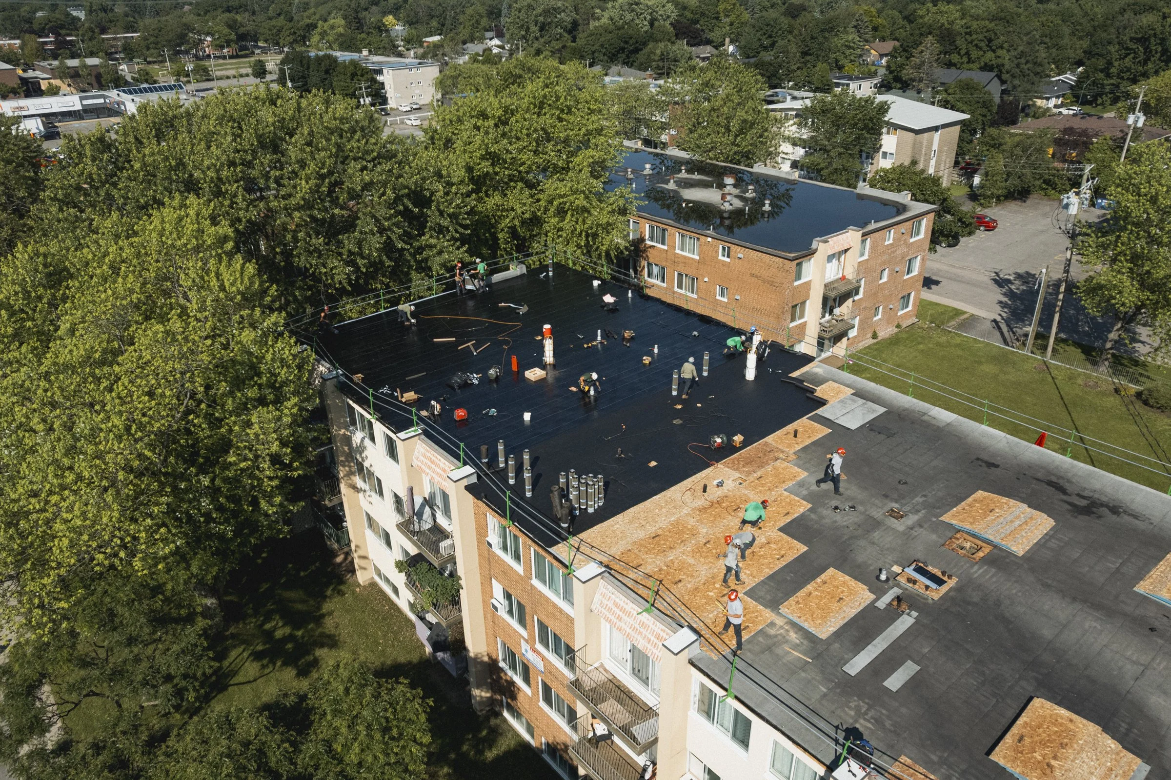 Travaux de rénovation de la toiture d'un immeuble résidentiel, avec des ouvriers travaillant sur la toiture et des outils dispersés.