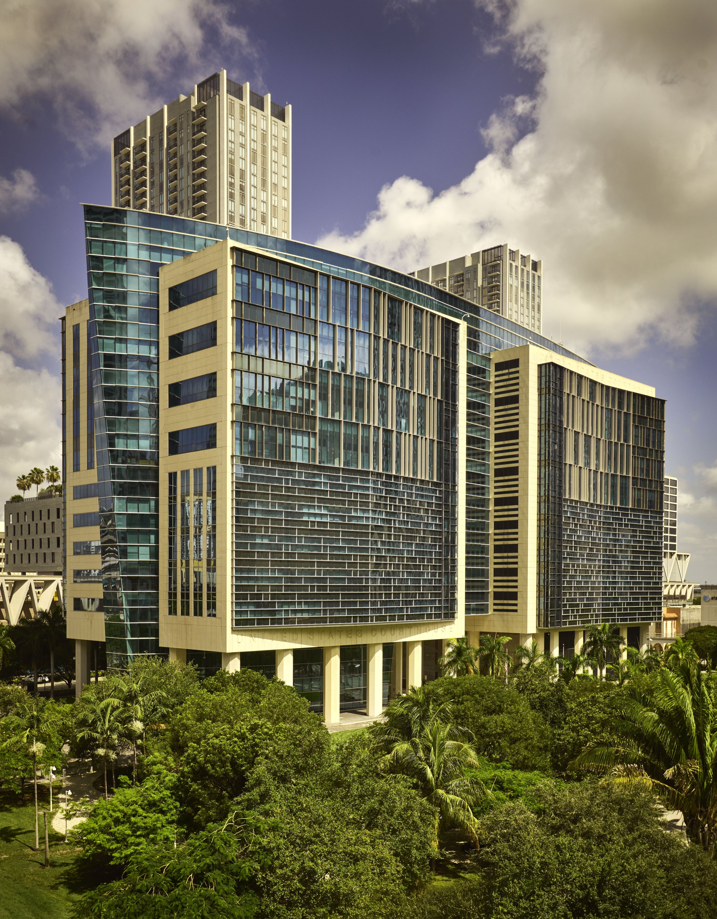 High-rise modern buildings with blue glass windows surrounded by lush green trees.