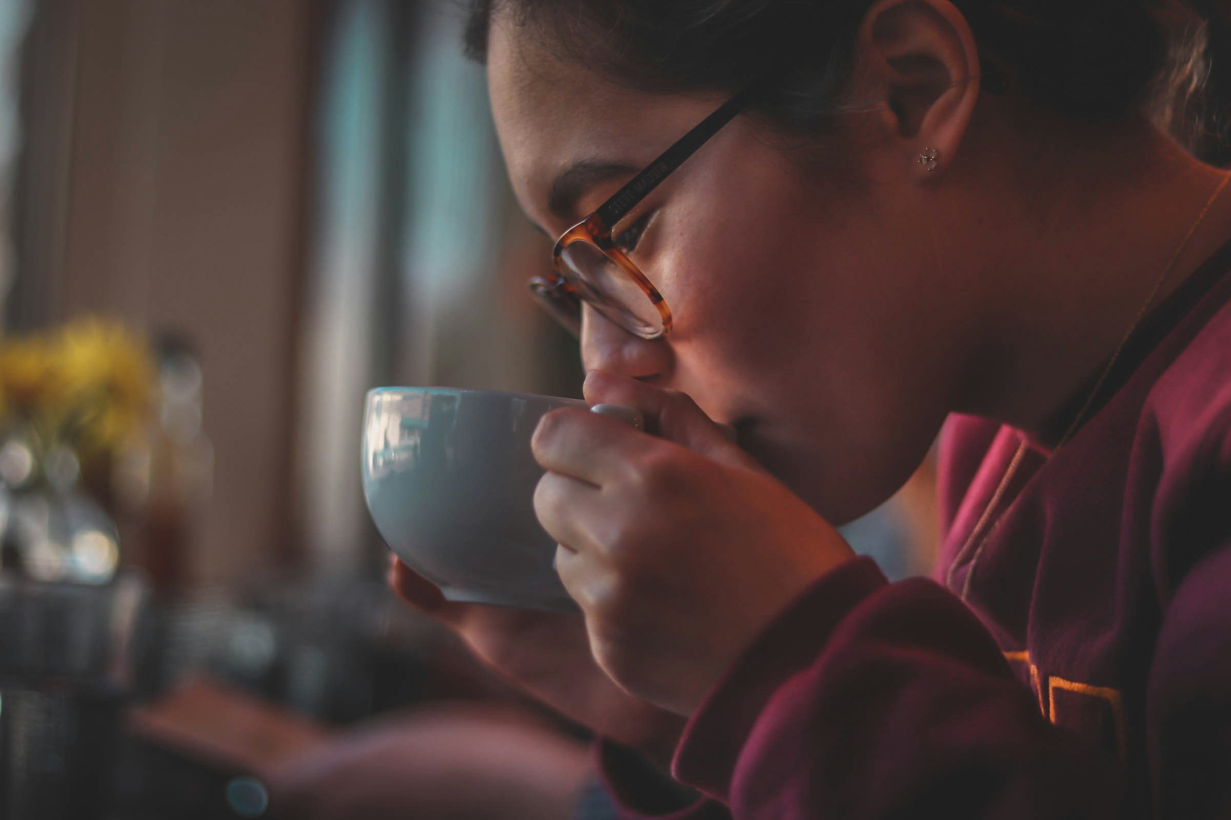 Person with glasses sipping a hot drink