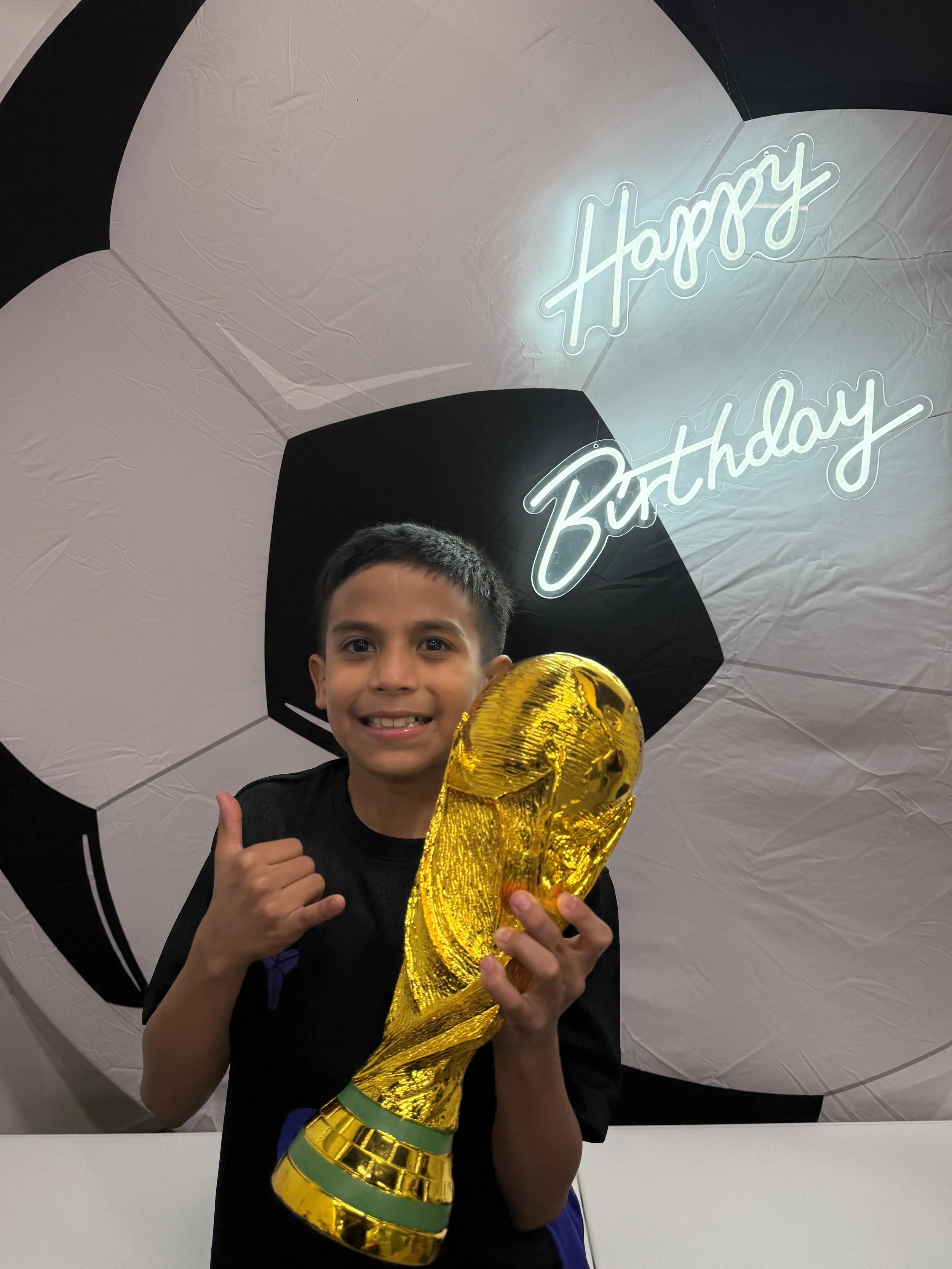 Three boys standing in front of wall decorations celebrating a 9th birthday, with soccer-themed artwork, a South African flag, and life-sized soccer player cutouts.