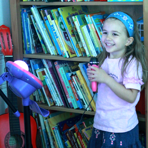Five-year-old girl smiling while holding a microphone during a speech therapy activity.