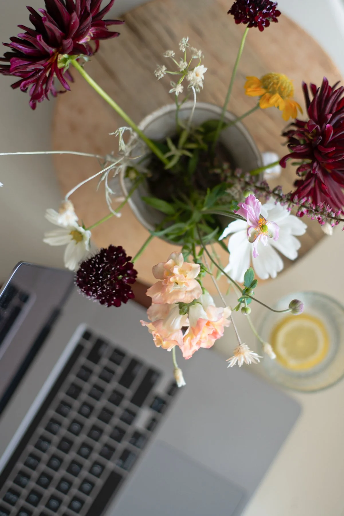 aerial view of a laptop with a vase of fresh flowers next to it as well as a glass of lemon water