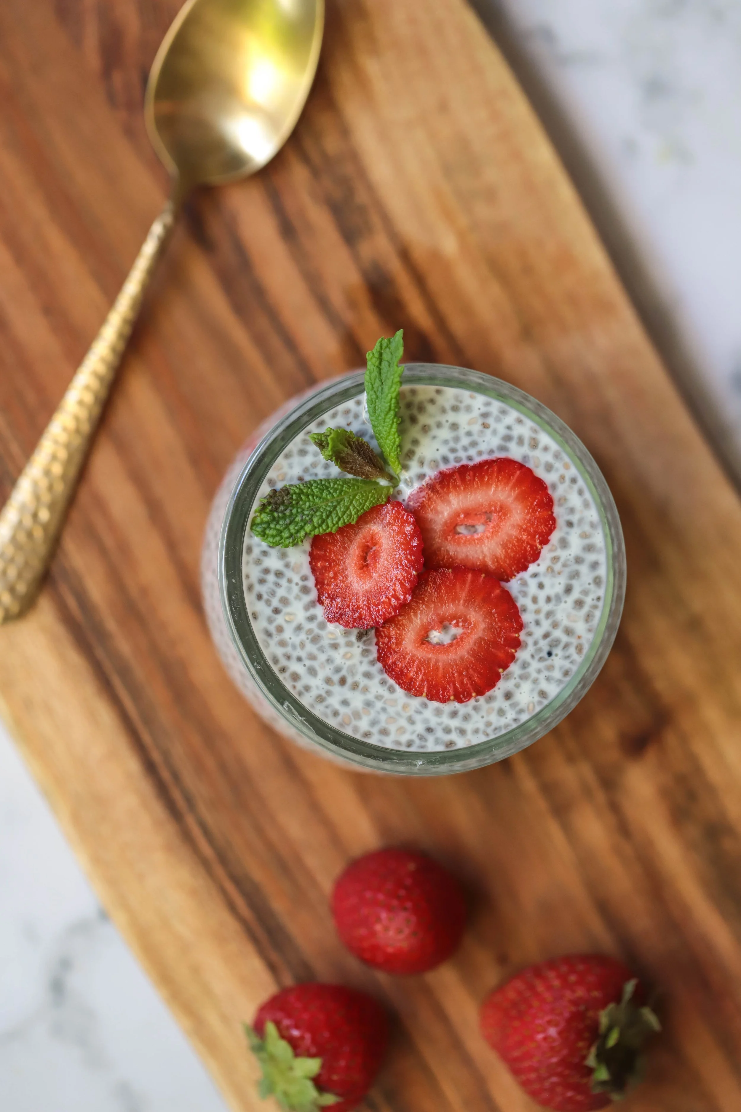 Chia seed pudding with strawberries and mint as garnish on cutting board with gold cutlery