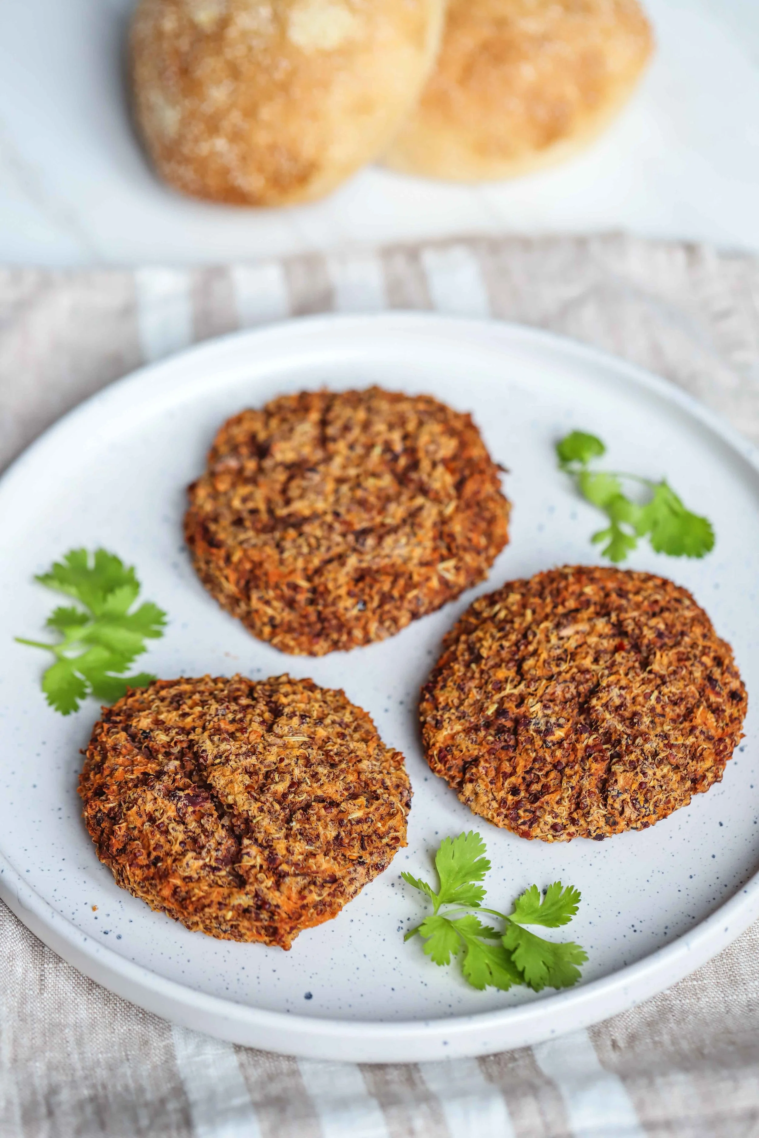 Quinoa bean and sweet potato burger on a white speckled plate with cilantro garnish on a linen napkin with a white stripe