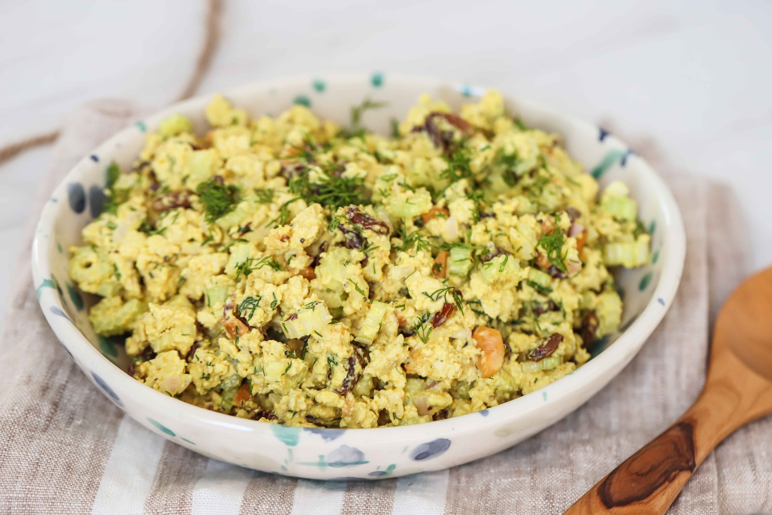 Bowl of curried tofu on a linen napkin next to a wooden spoon