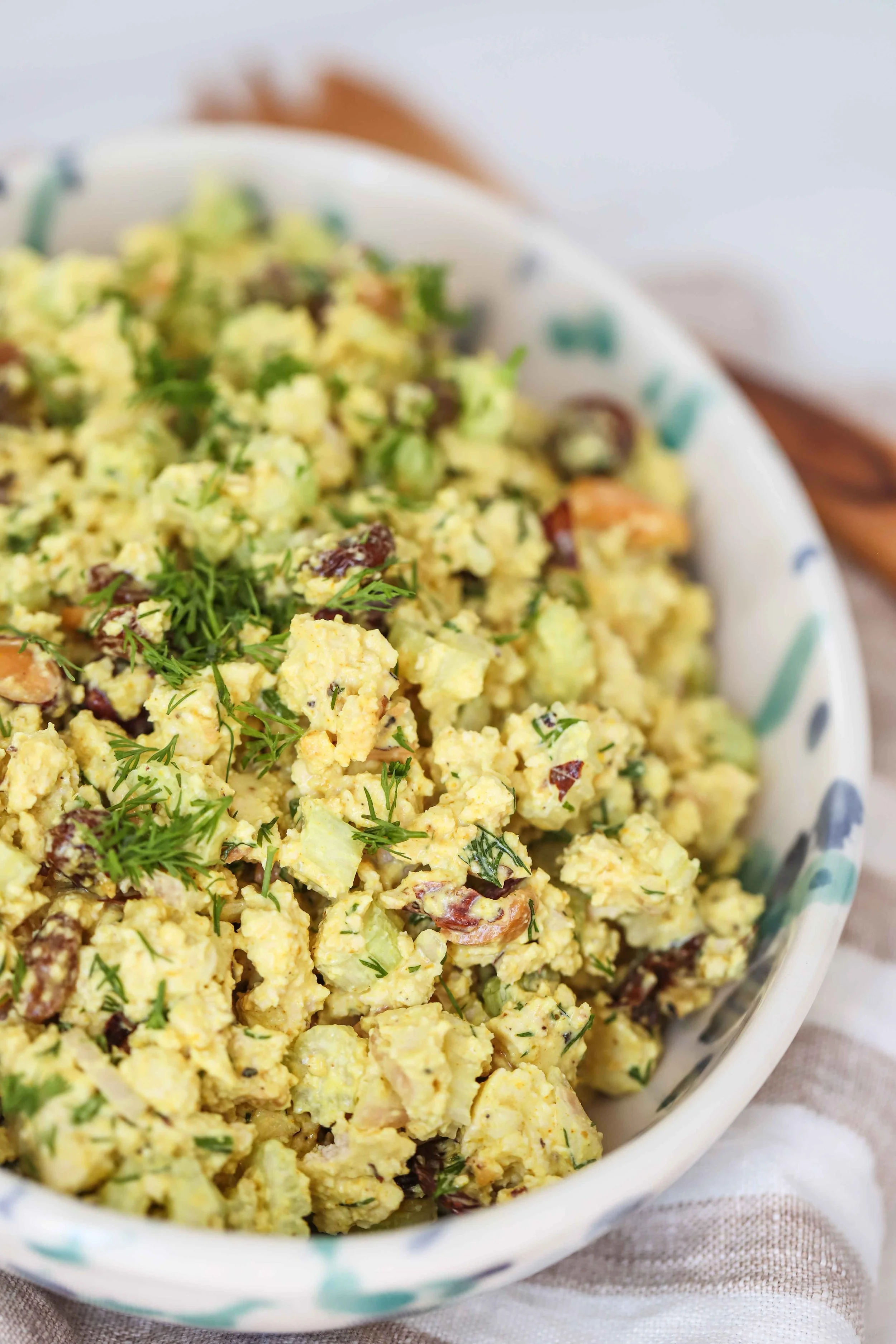 Bowl of curried tofu on a linen napkin next to a wooden spoon