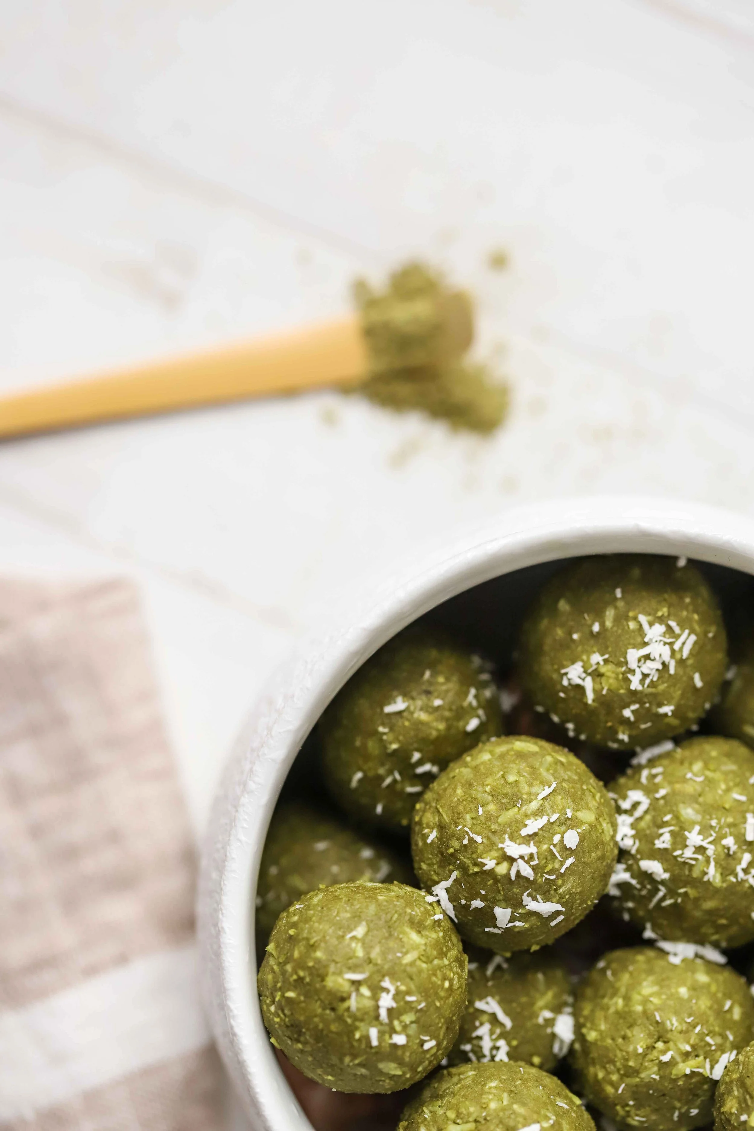 Coconut Matcha Energy Bites in a white bowl on a white countertop next to a linen napkin