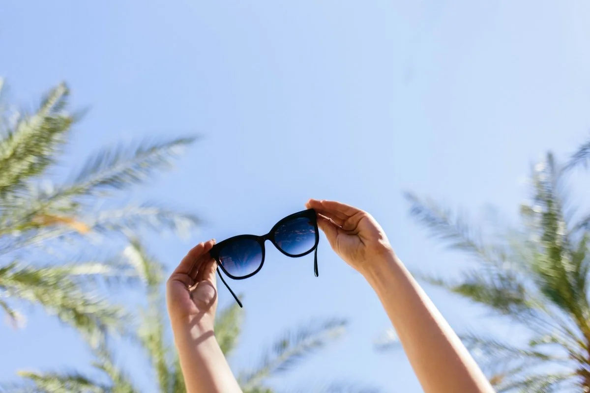 sunglasses held up by a woman to the sky representing the role of light in wellness and how it affects circadium rhythm and sleep quality