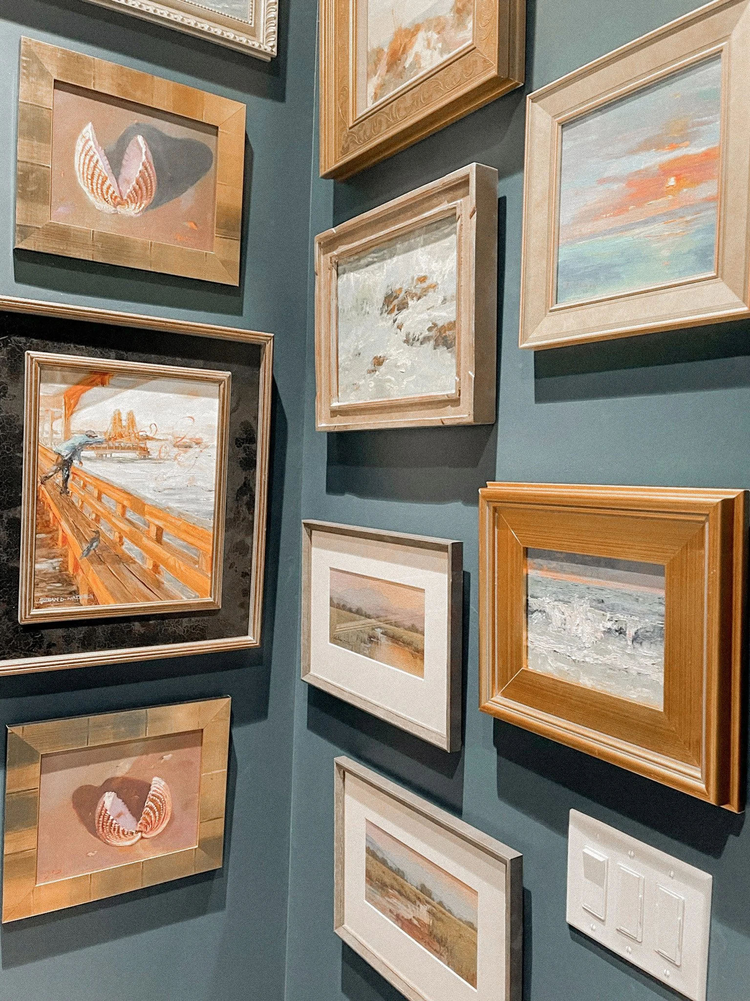 Curated gallery wall featuring framed coastal artwork against deep teal walls, creating a layered, elevated interior design moment.