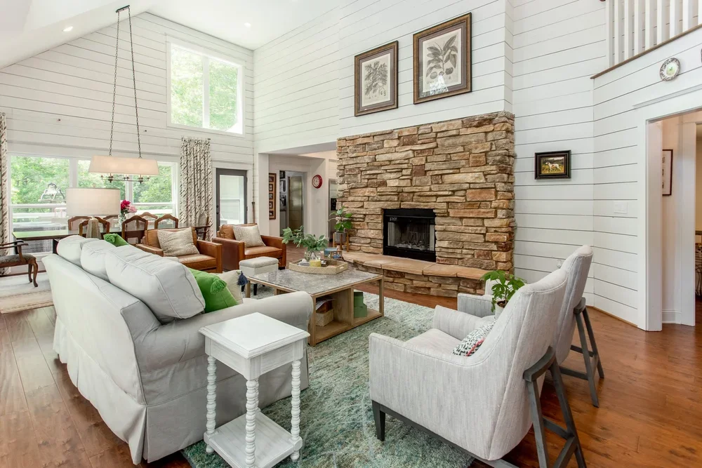 A bright, inviting living room renovation featuring a natural stone fireplace, vaulted shiplap walls, warm wood accents, and timeless finishes designed for comfortable everyday living.