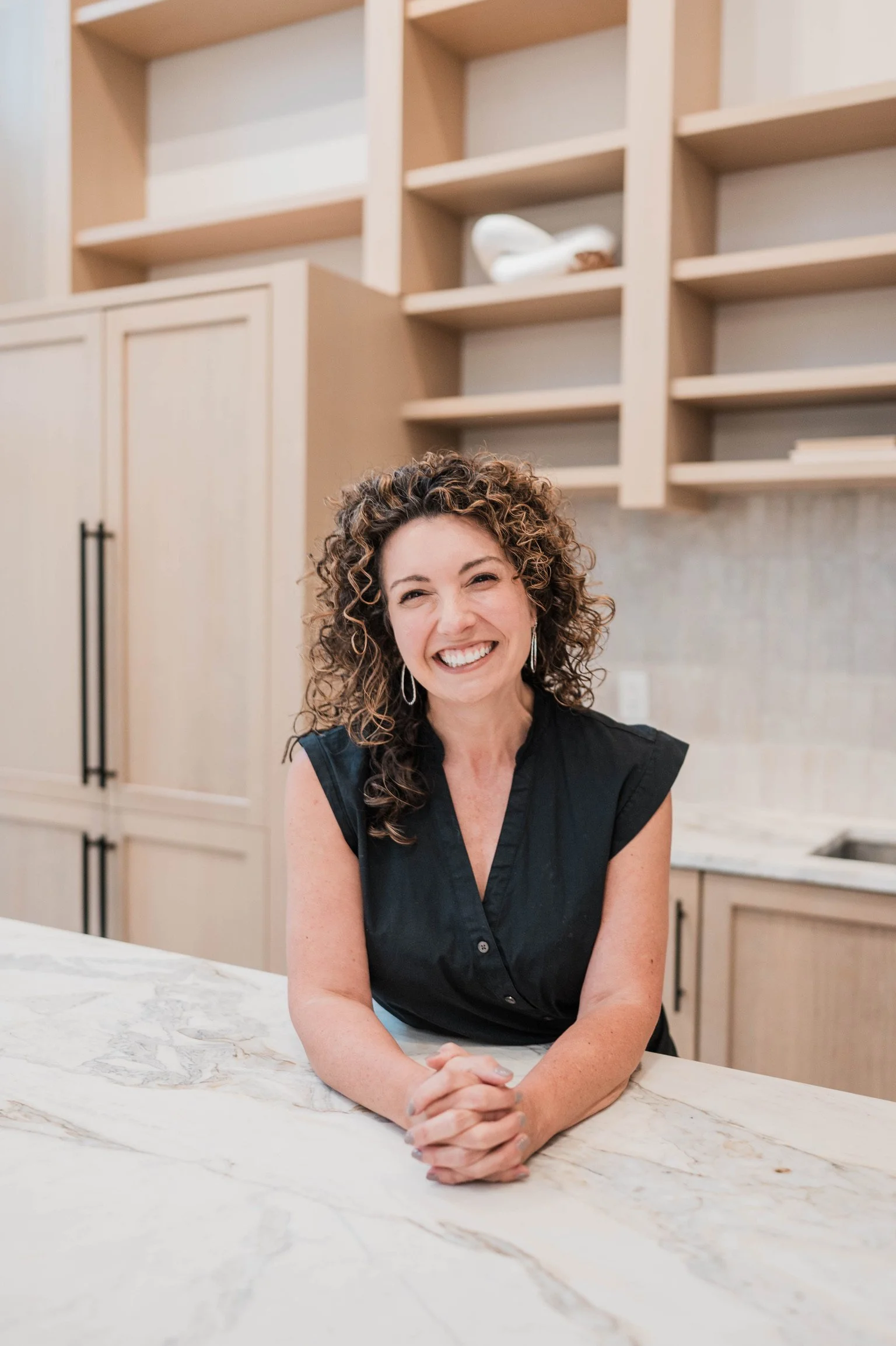 Betsy Manley, luxury interior designer and home renovation expert, in a custom kitchen featuring warm wood cabinetry and marble countertops.